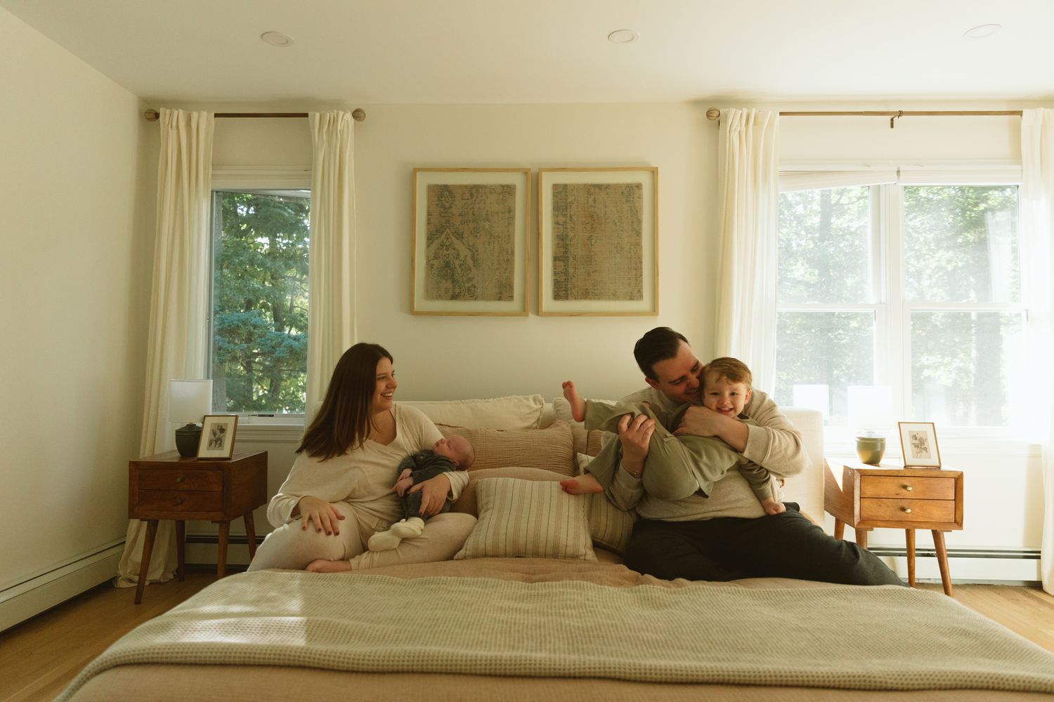 Family relaxing together on a large bed in a bright, modern bedroom with white walls and natural light.