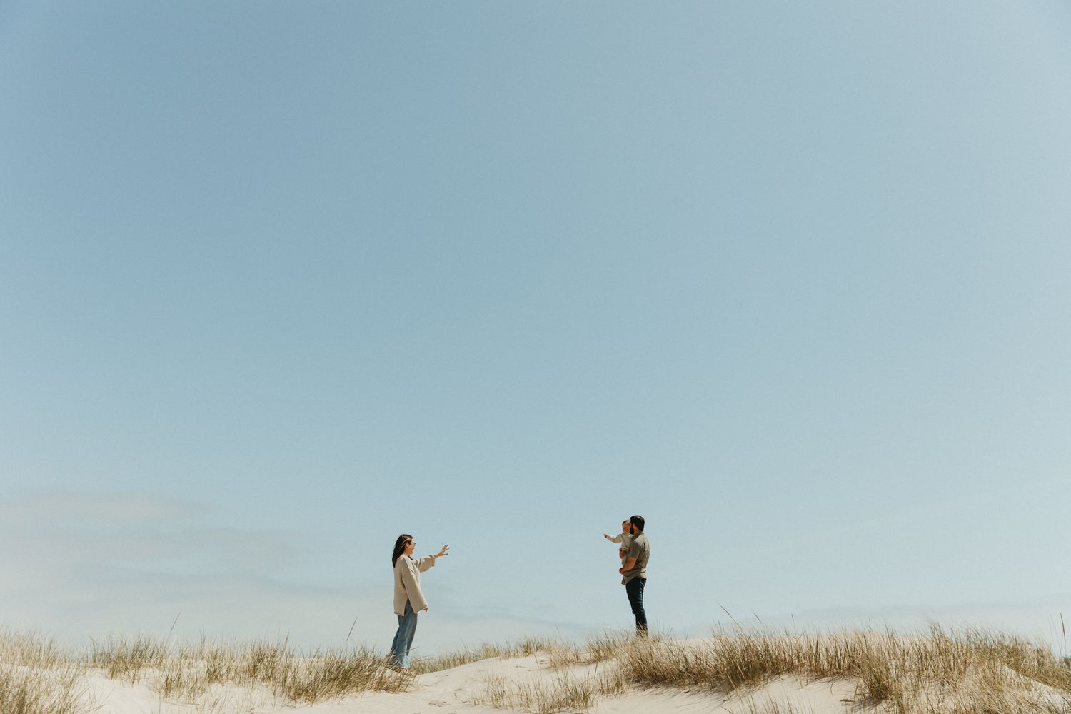 People exploring sandy dunes against bright blue sky.