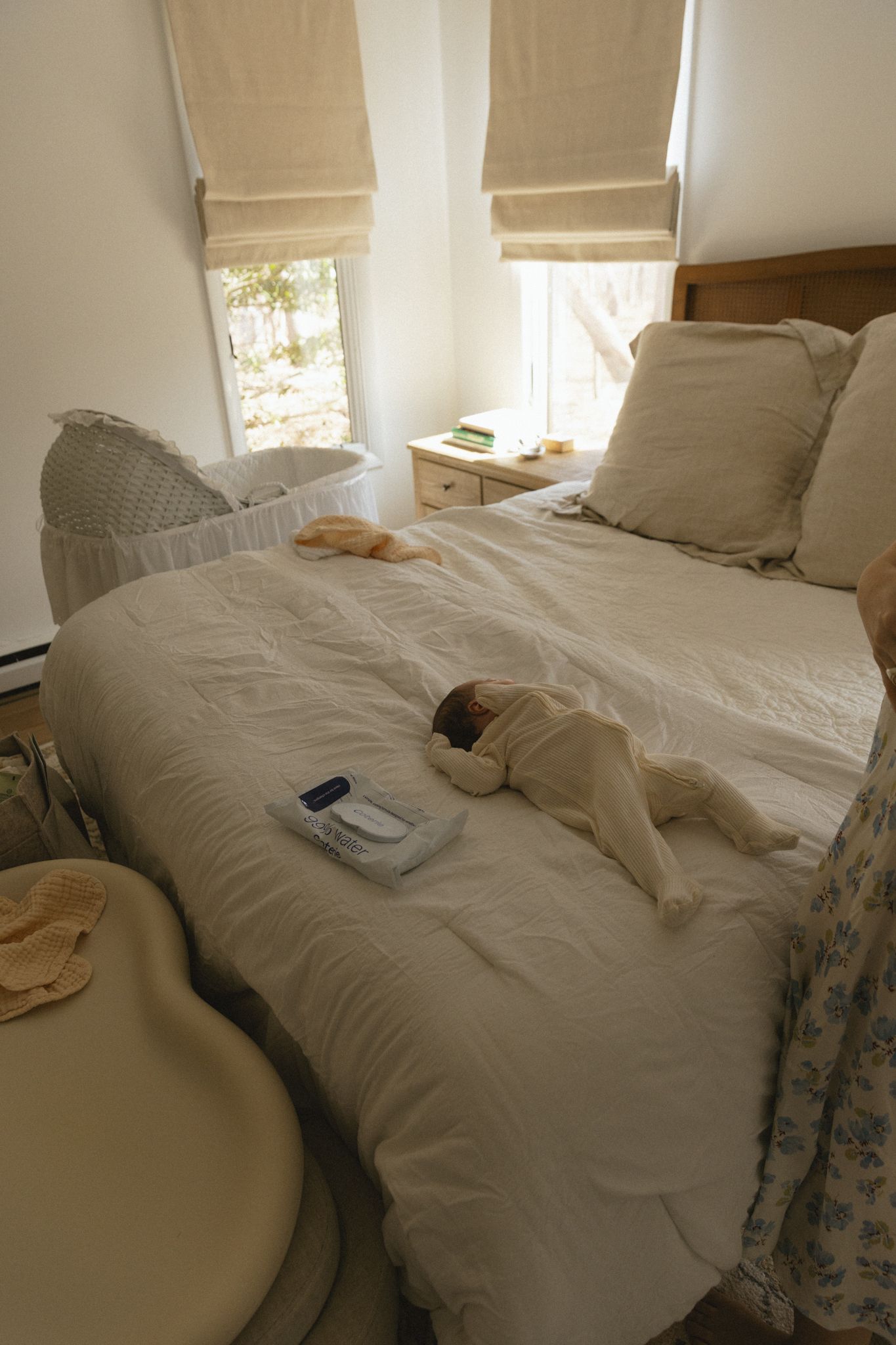 Cozy bedroom interior with white bedding, beige roman shades, and natural light streaming through windows.