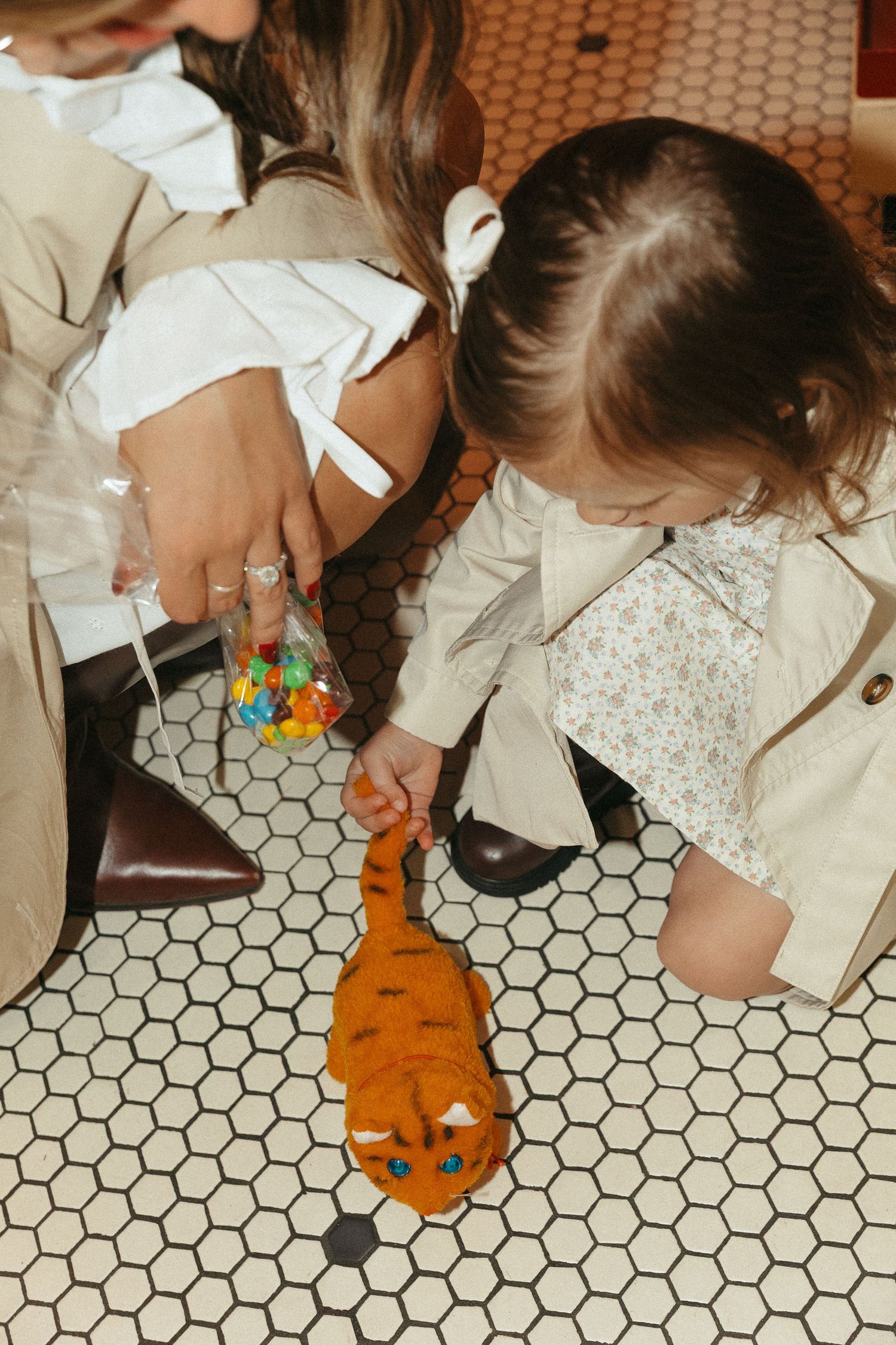 Small stuffed tiger toy on white hexagonal tile floor next to beige coat.