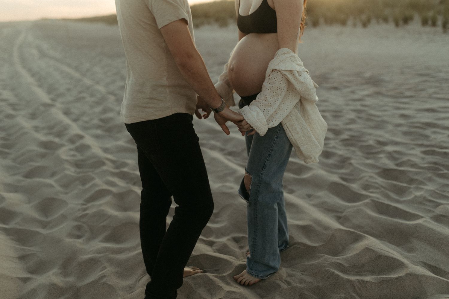 Couple walking hand in hand on sandy beach at dusk.