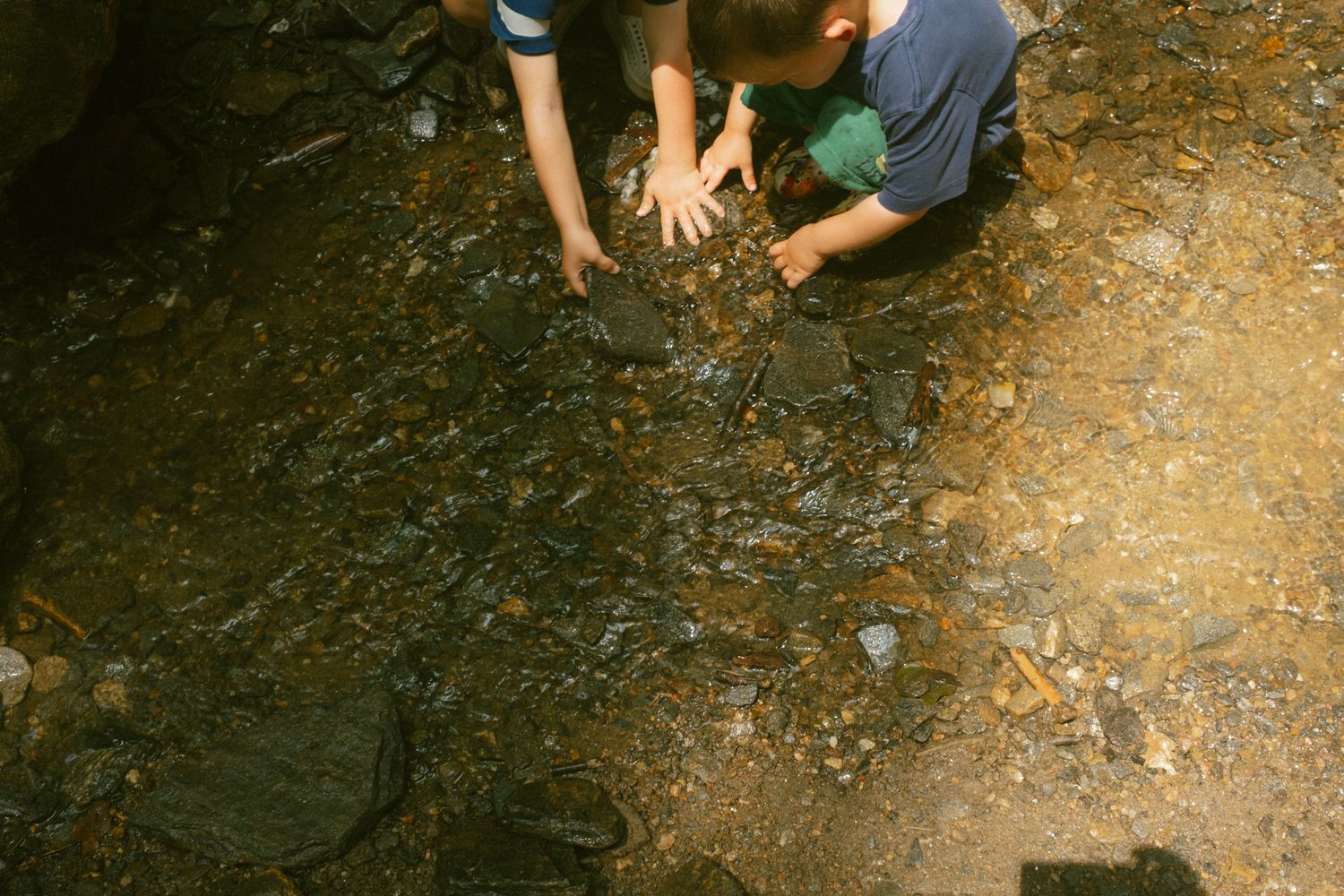 Two children examining rocks and pebbles along a rocky creek bed outdoors.