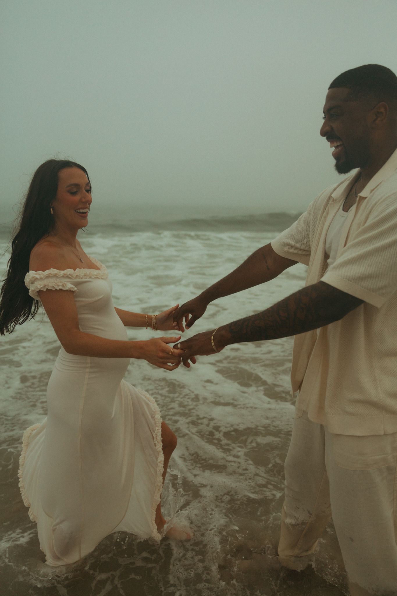 Romantic couple in white outfits dancing together on a misty beach.