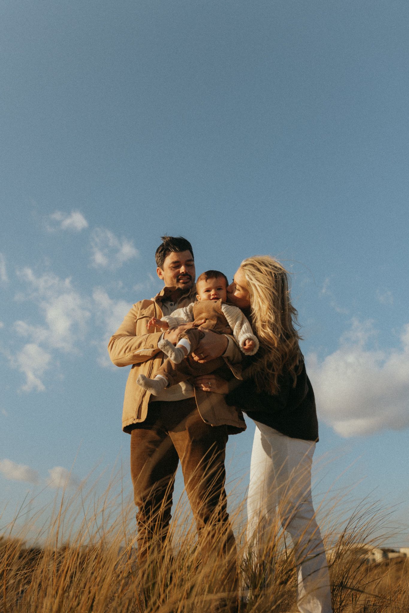 People enjoying a playful moment together against a blue sky and tall grass backdrop.
