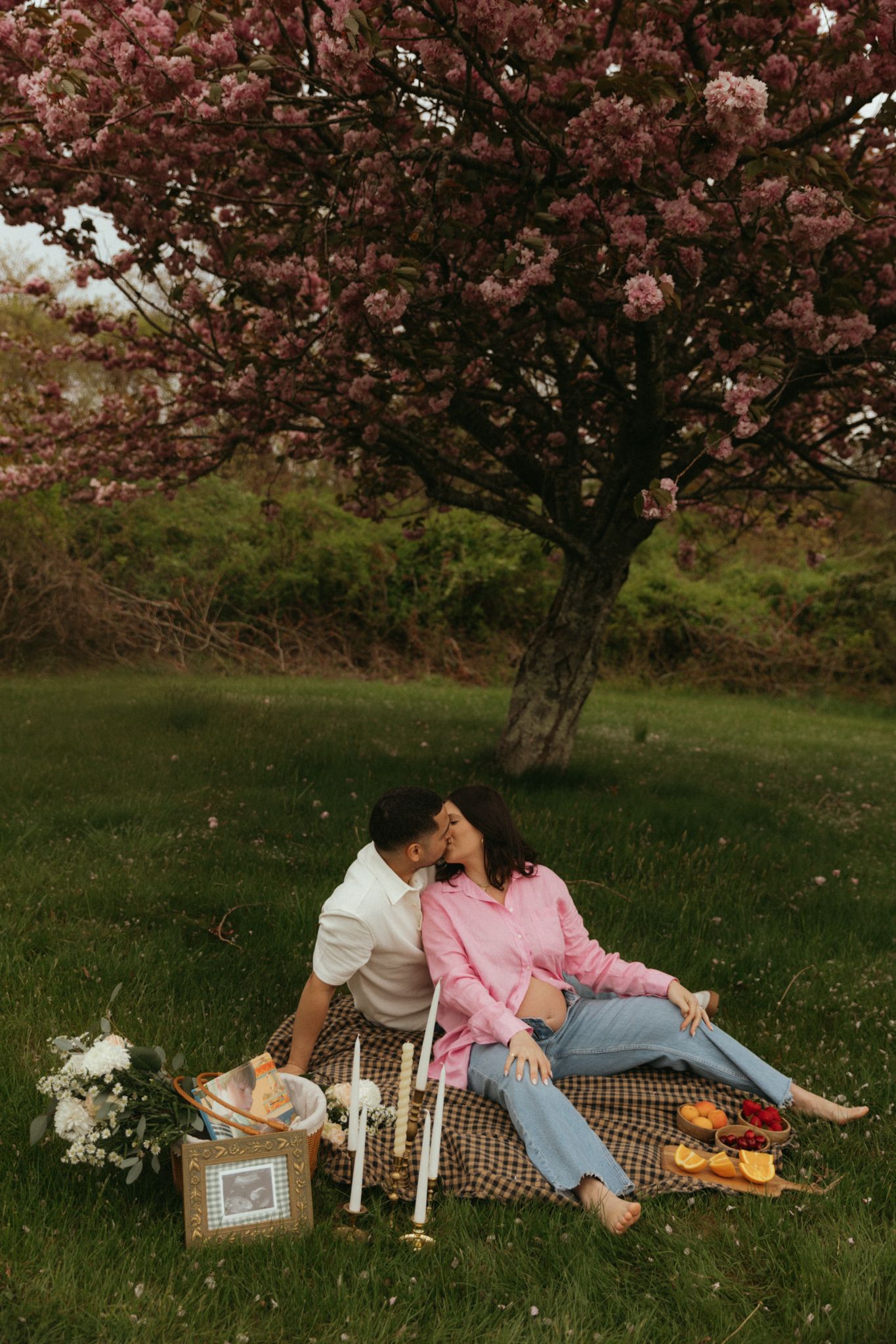 A romantic picnic setup under blooming cherry blossom trees with candles and snacks.