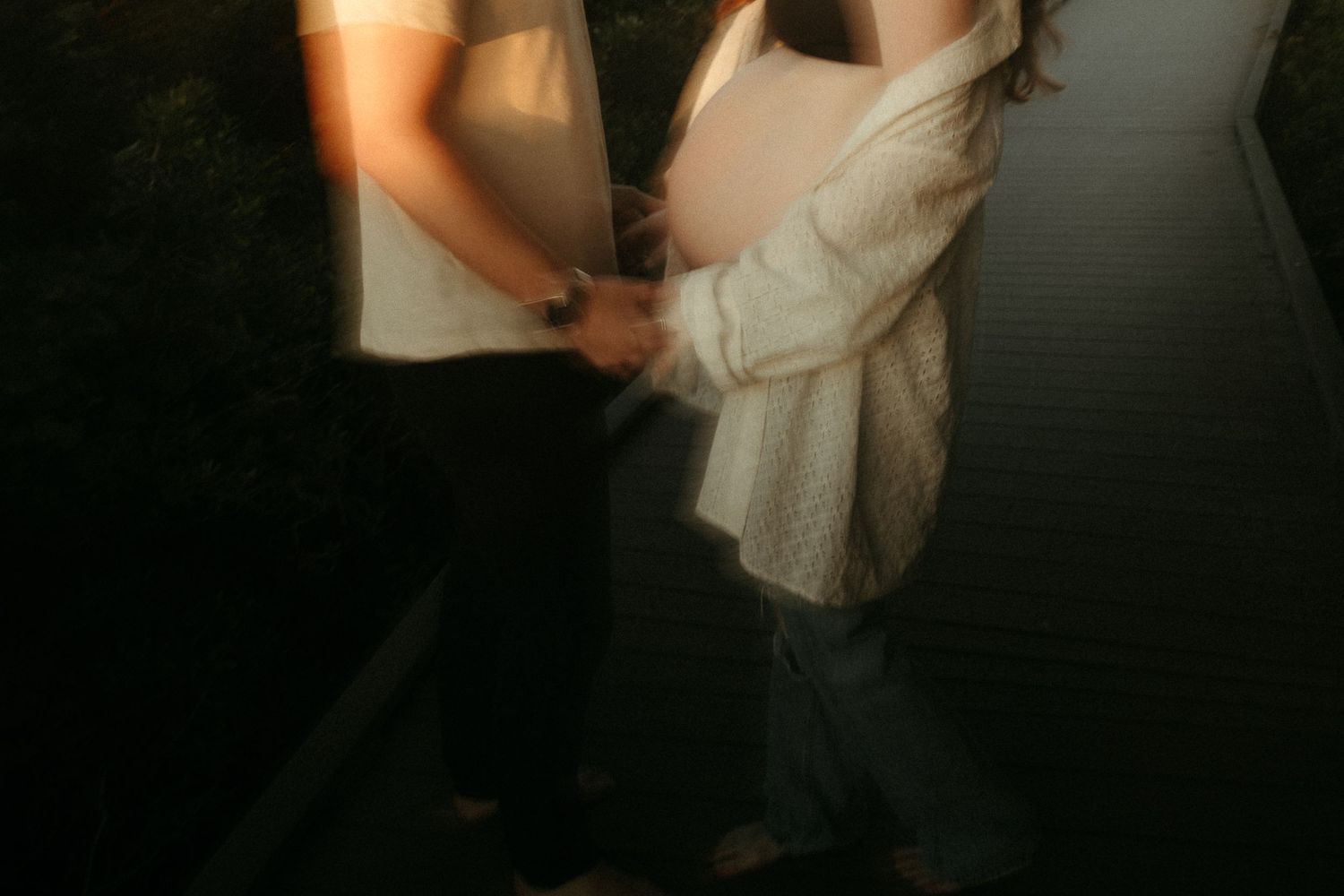 A couple holds hands and dances playfully together on a dark beach at night.