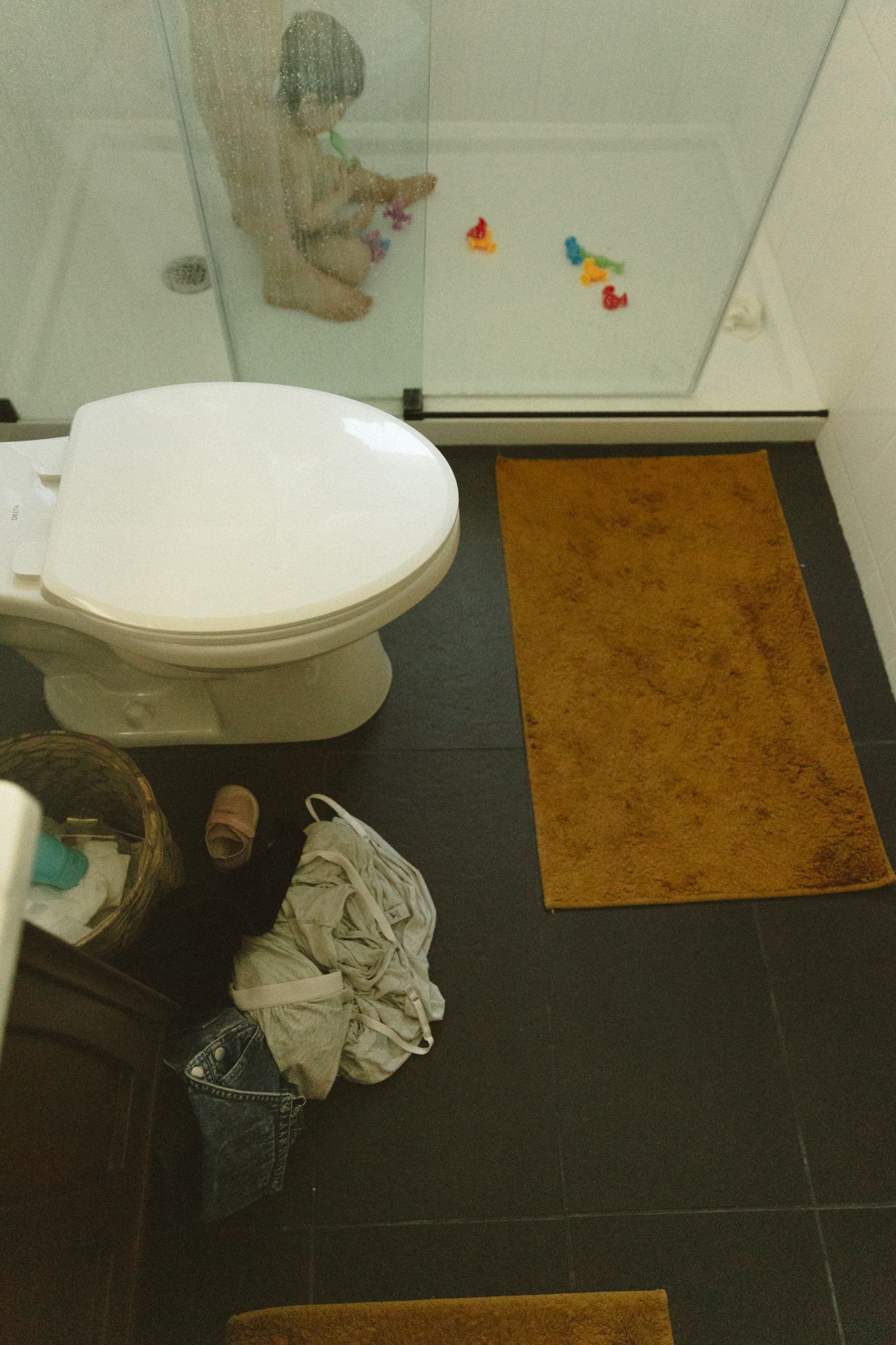 Black and white bathroom tiles with a white toilet and brown bath mat.