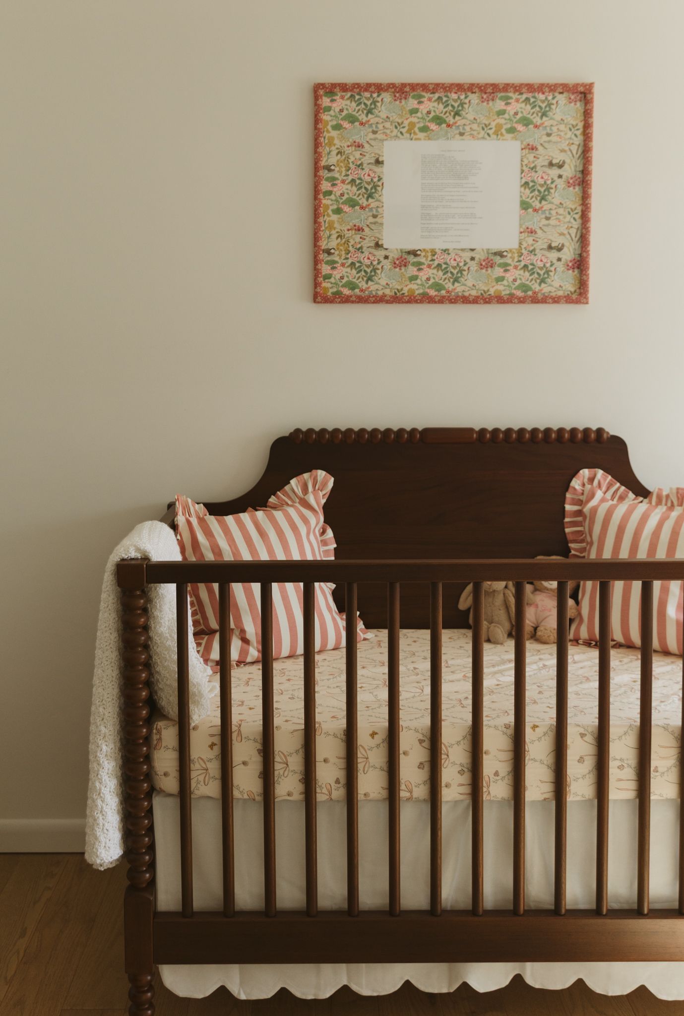 Dark wooden crib with floral accents and striped pillows in a minimalist nursery setting.