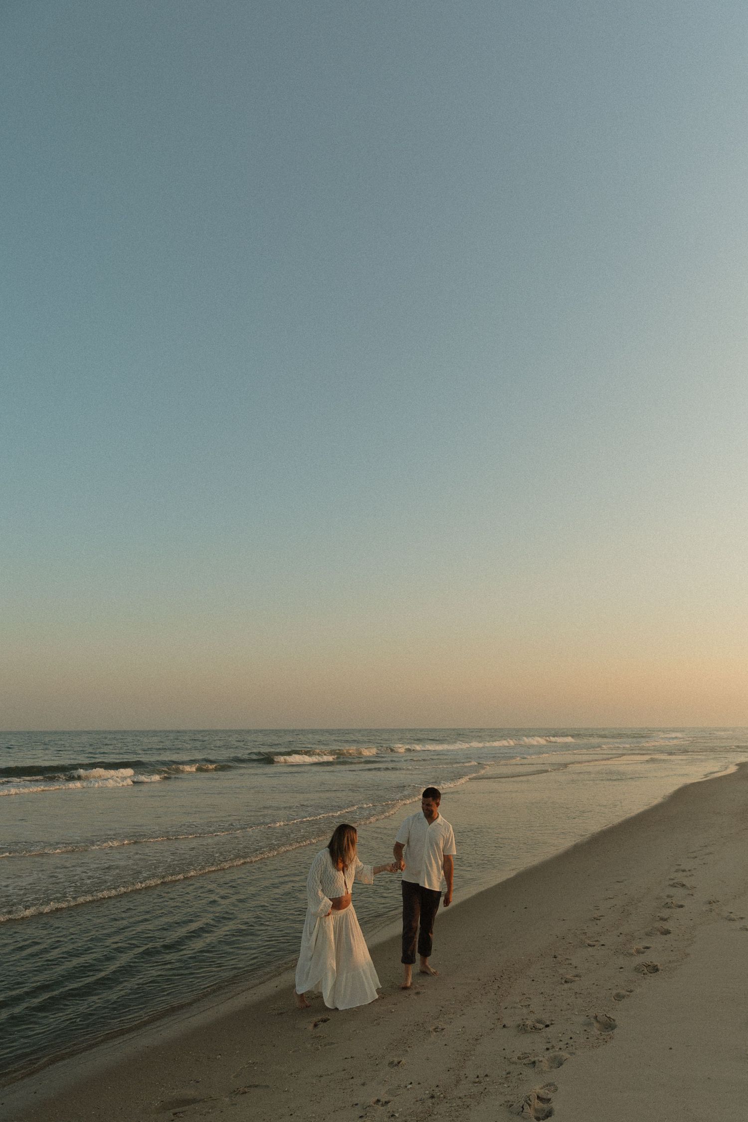 A serene beach scene at sunset with figures walking along the shoreline.