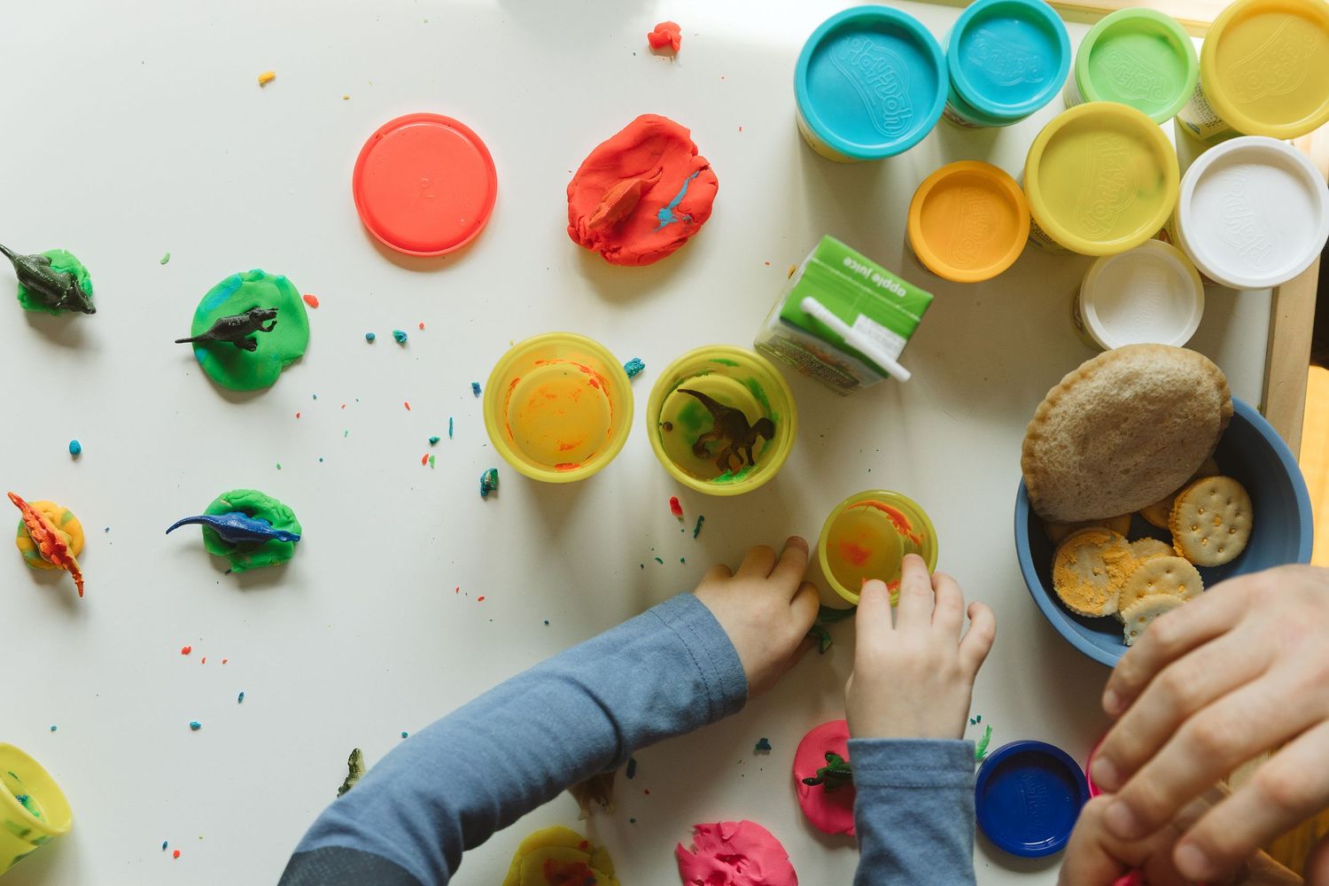 Child playing with colorful Play-Doh containers and clay creations spread on a white table.
