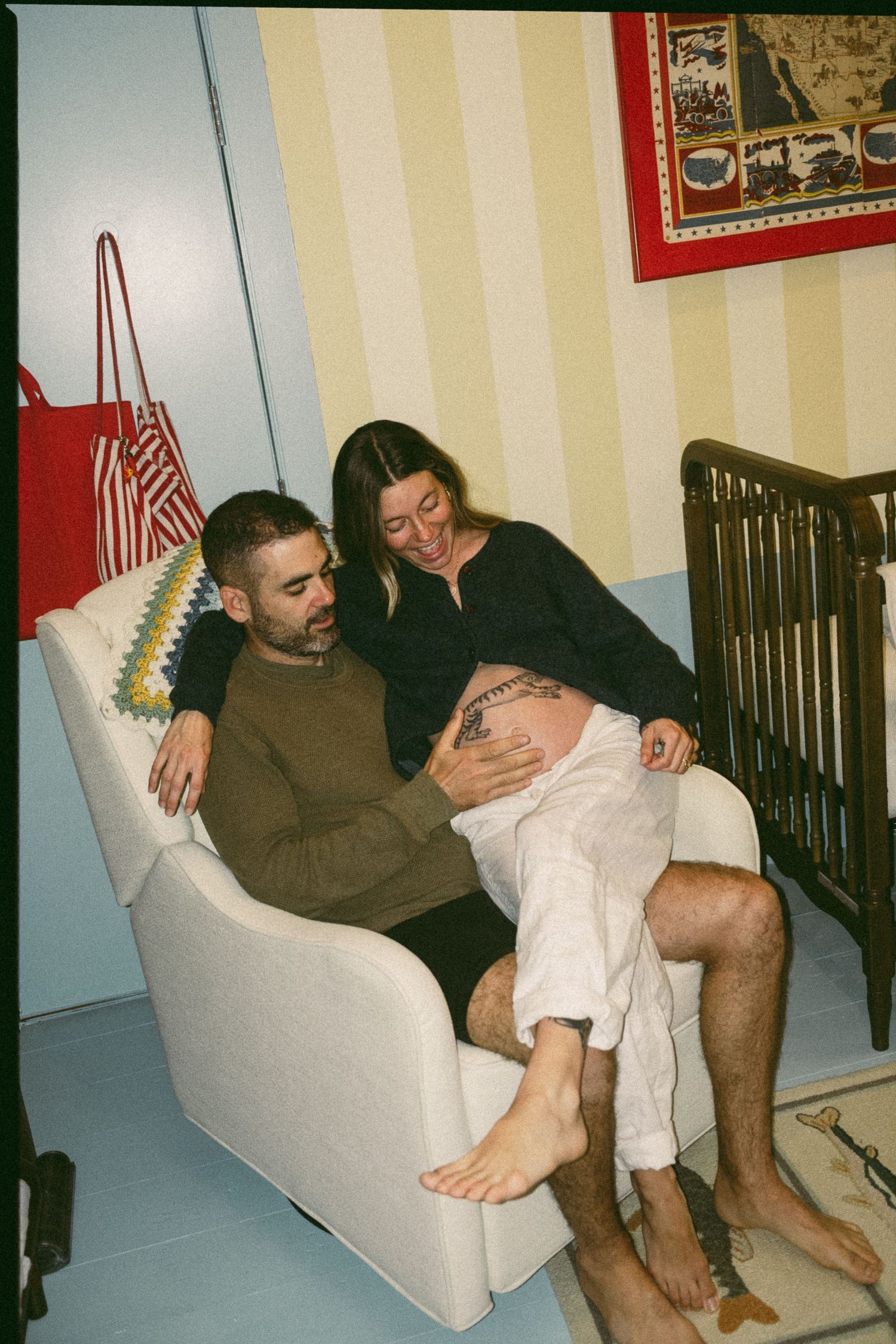Couple in nursery chair tenderly touching pregnant belly near baby crib.