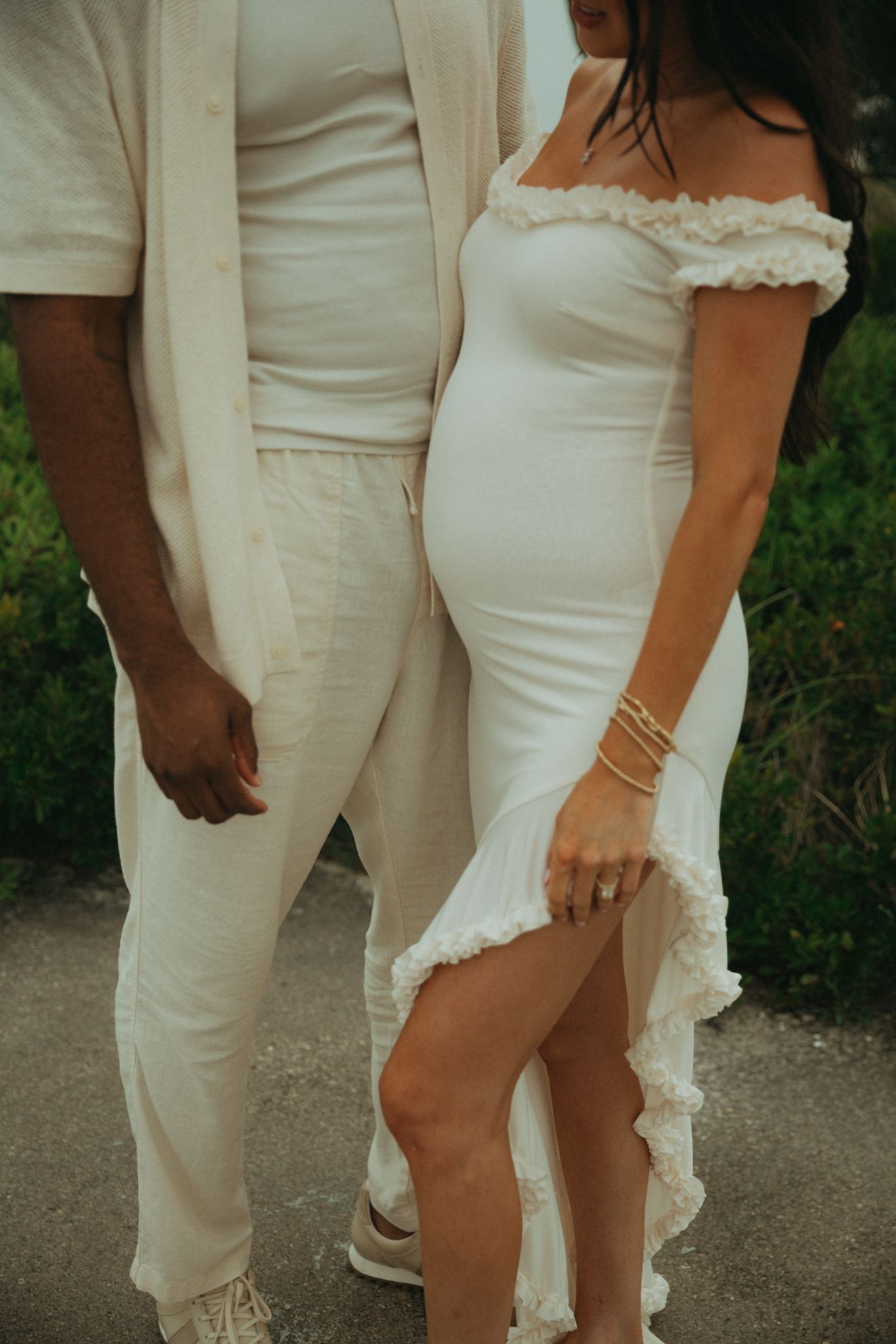 Couple in matching white outfits standing together on a beach path.