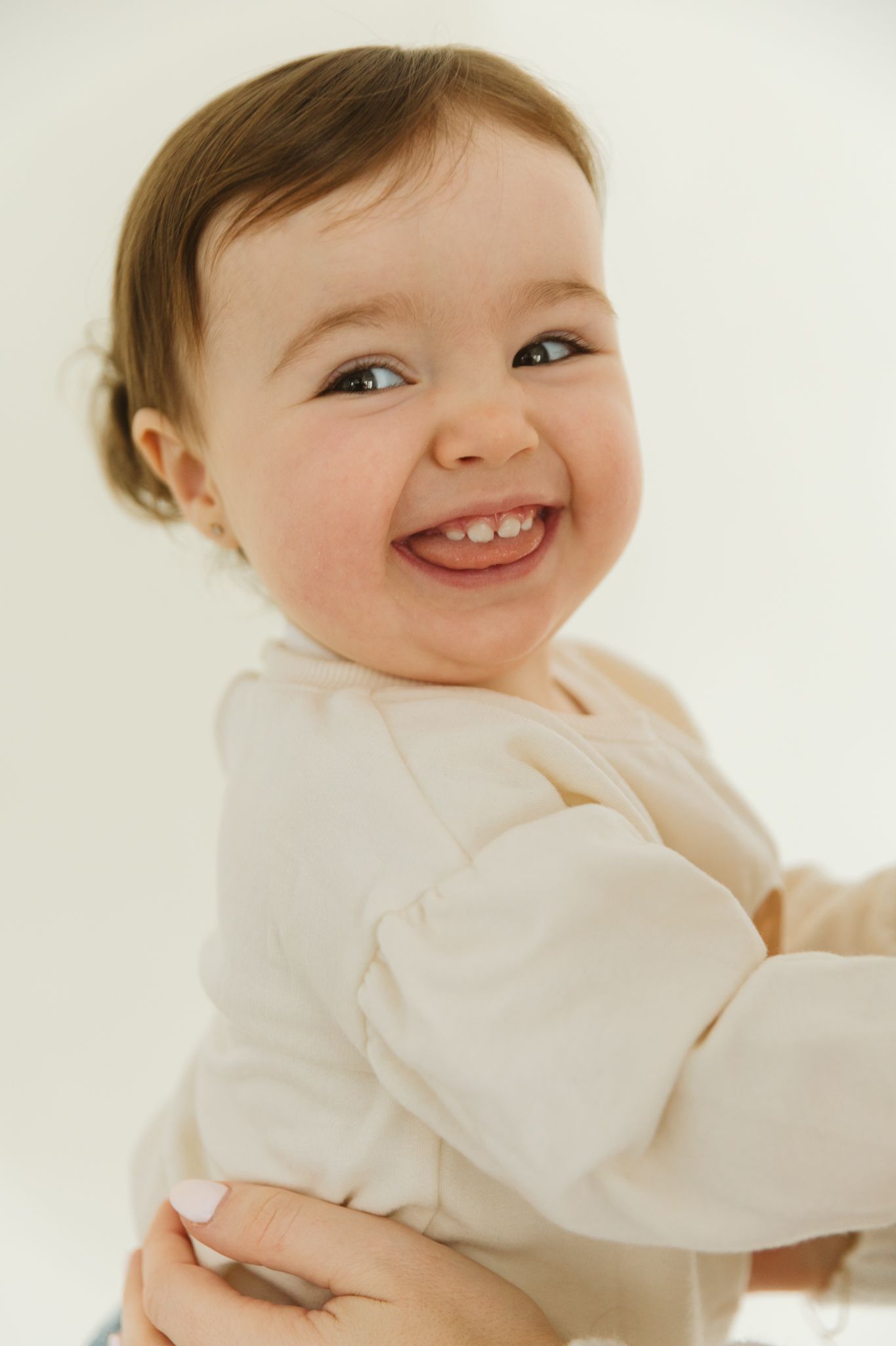 Close-up portraits of a smiling baby in white clothing against a bright background.