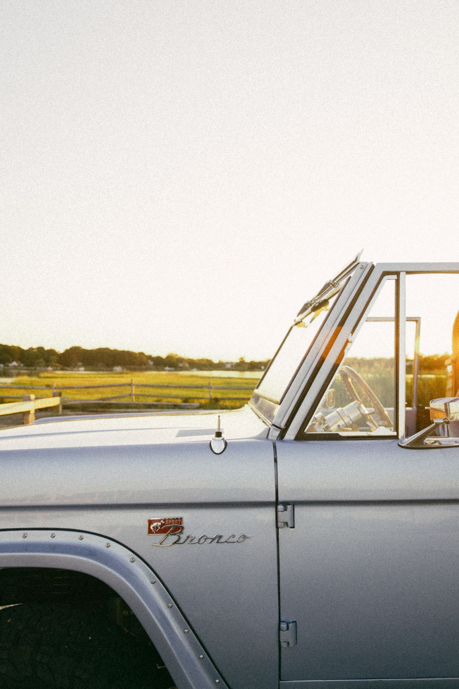 Vintage Ford Bronco in light blue parked at golden hour sunset, classic American off-road vehicle side profile view.
