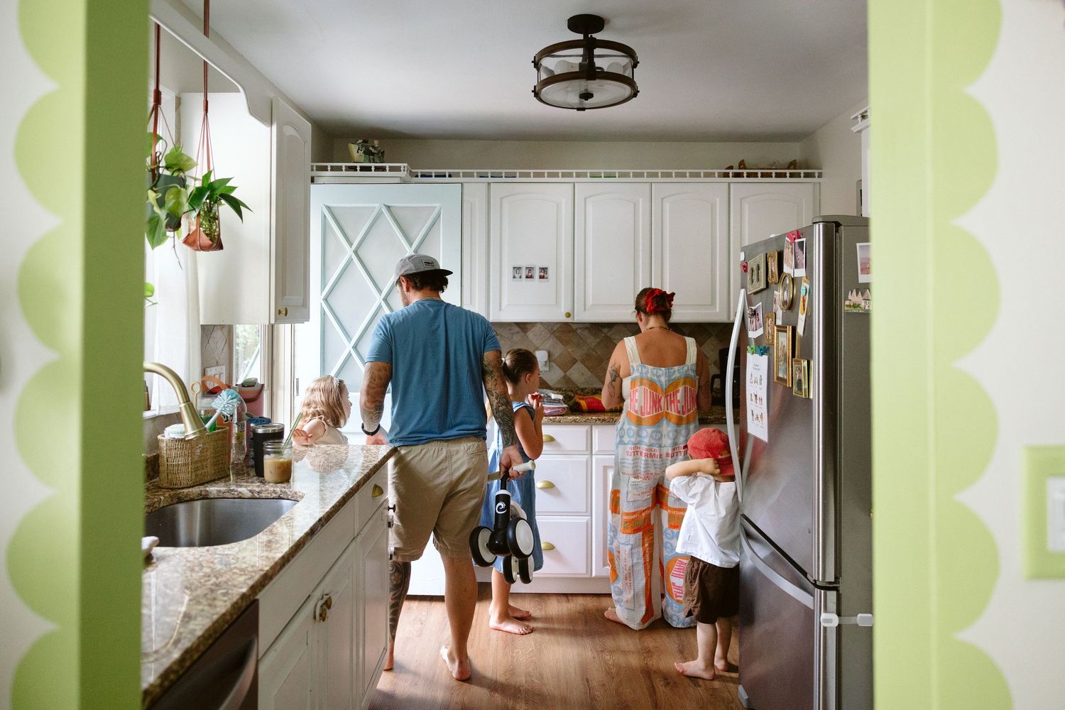 Family gathered in a bright, cozy kitchen with white cabinets, green accents, and hardwood floors.