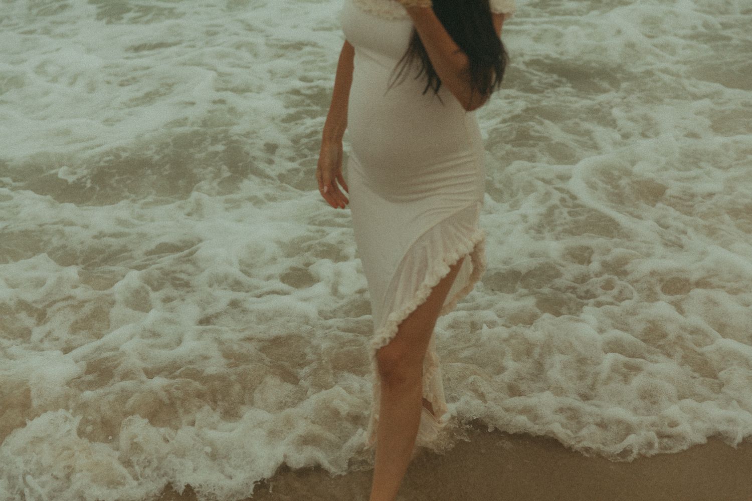 People playing in ocean waves wearing light colored dresses.