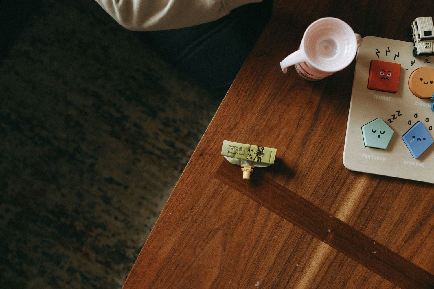 Overhead view of a wooden table with small decorative pins, a white mug, and a tray of cute button-shaped cookies.