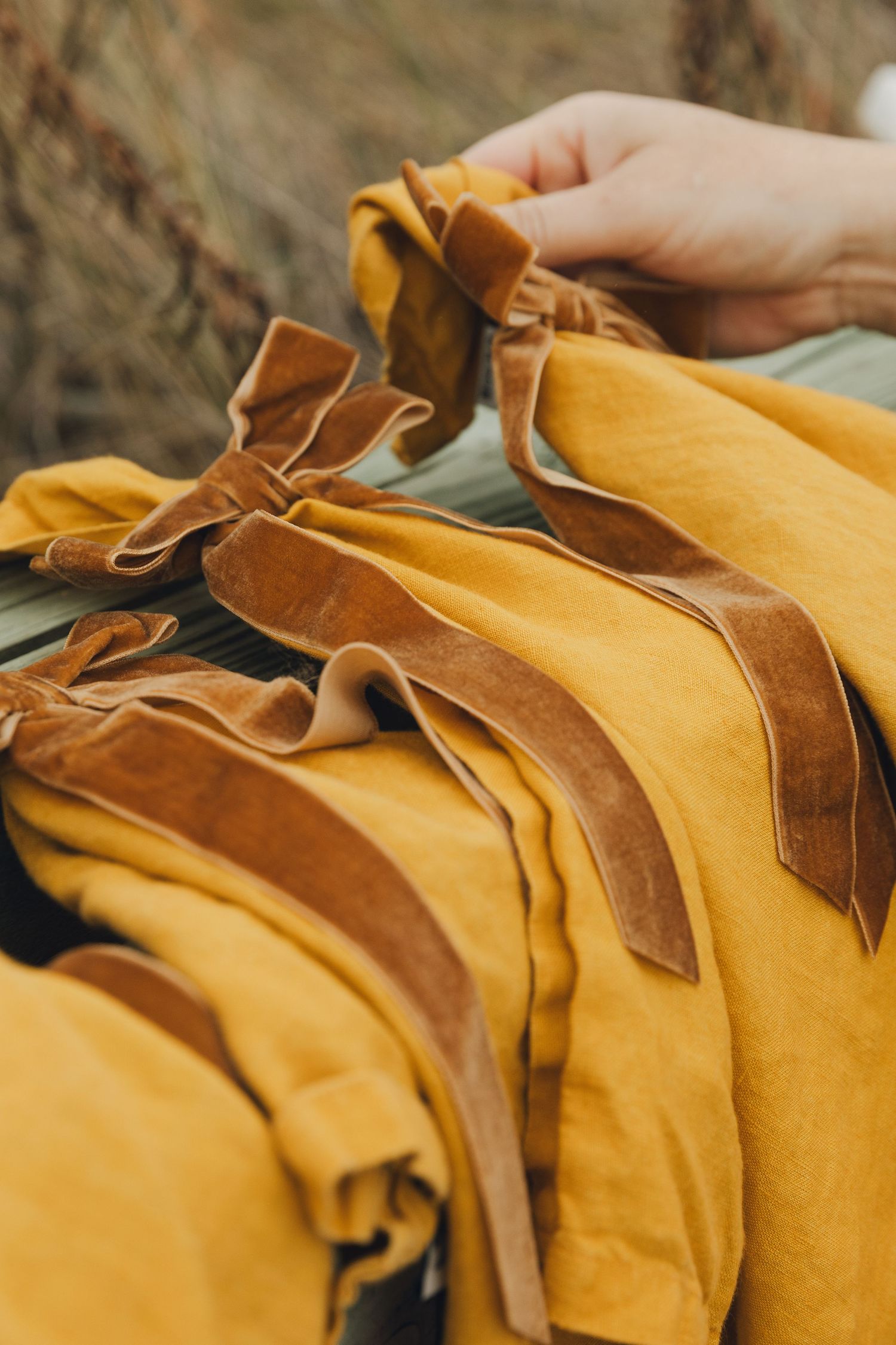 Mustard yellow linen garments with brown velvet ribbon ties displayed on a rack outdoors.