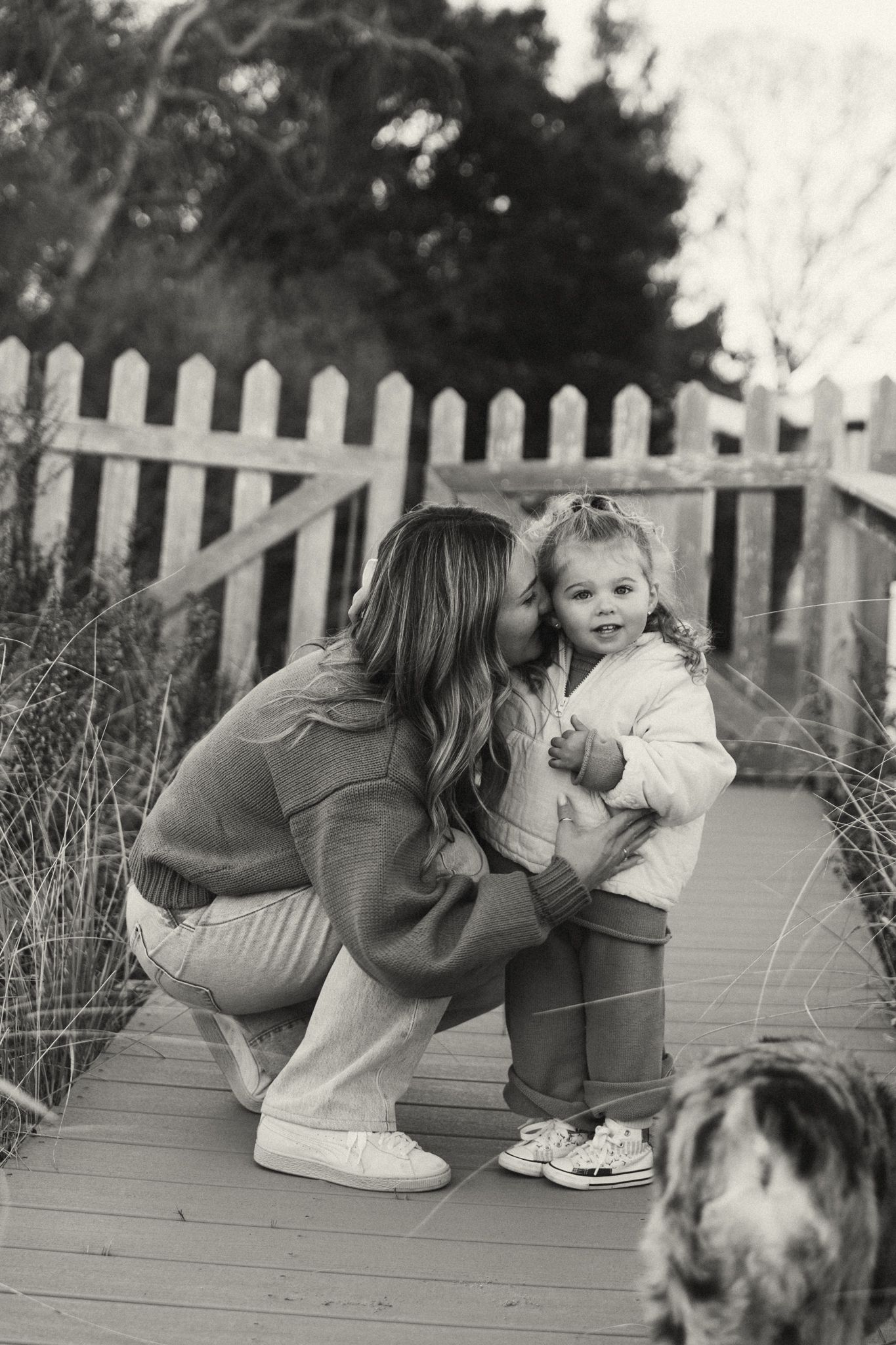 A sequence of intimate black and white photos showing affectionate moments on a wooden deck with a white picket fence.