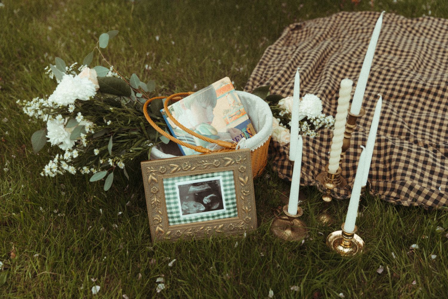 A vintage picnic setting with white candles and a checkered blanket in nature.
