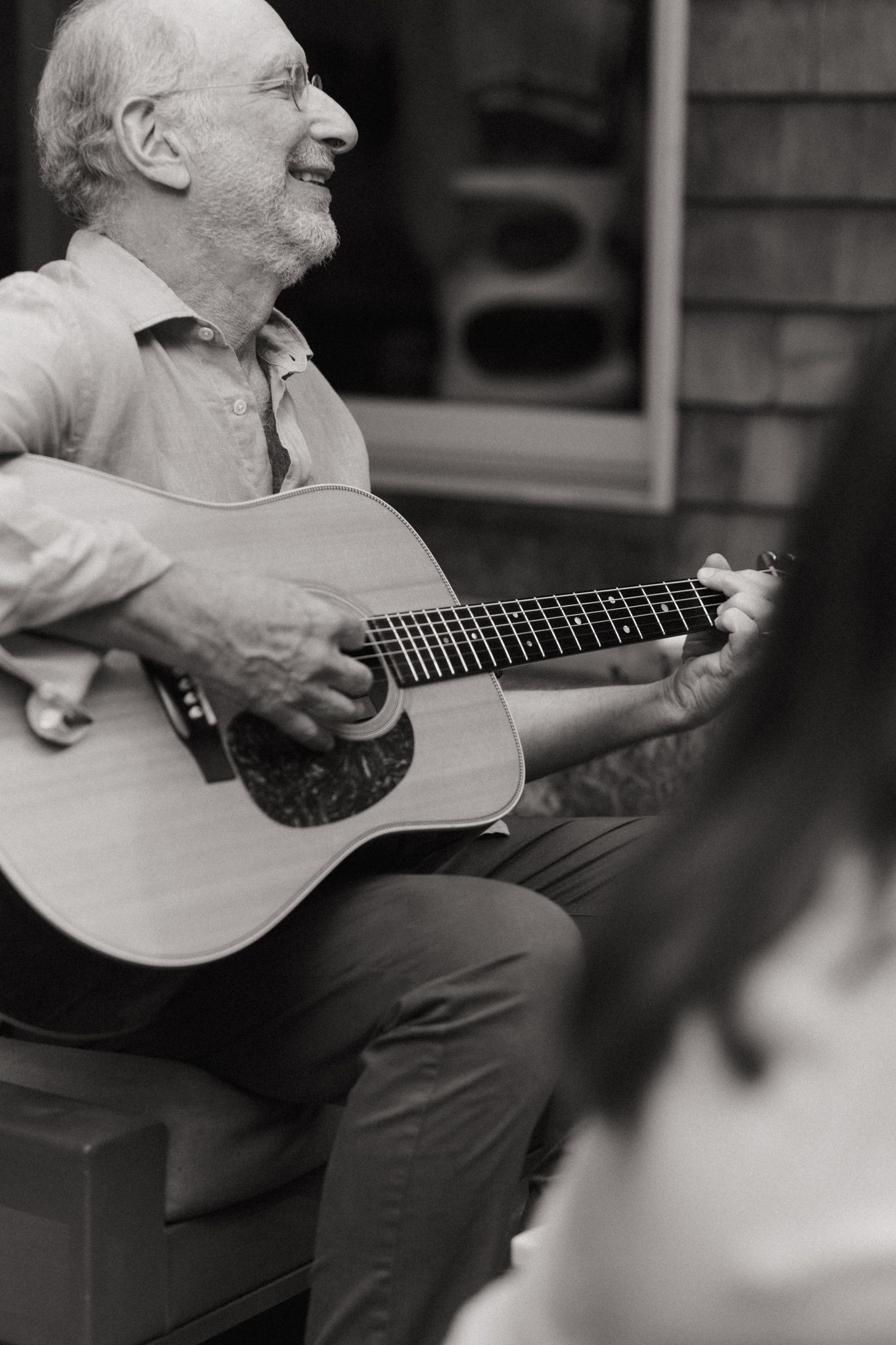 Person playing acoustic guitar while sitting outdoors in black and white photography.