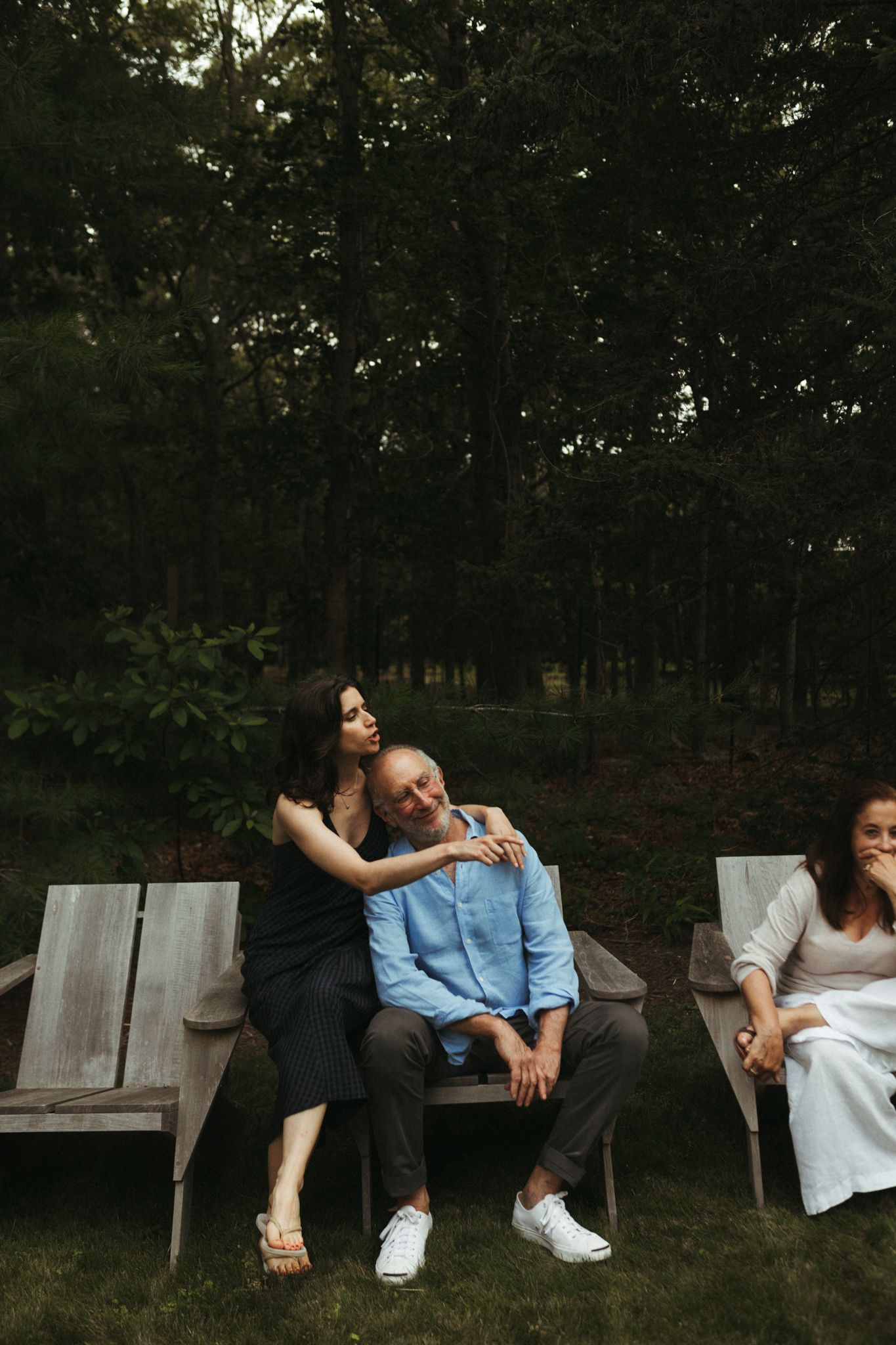 People relaxing on wooden benches in a wooded outdoor setting.