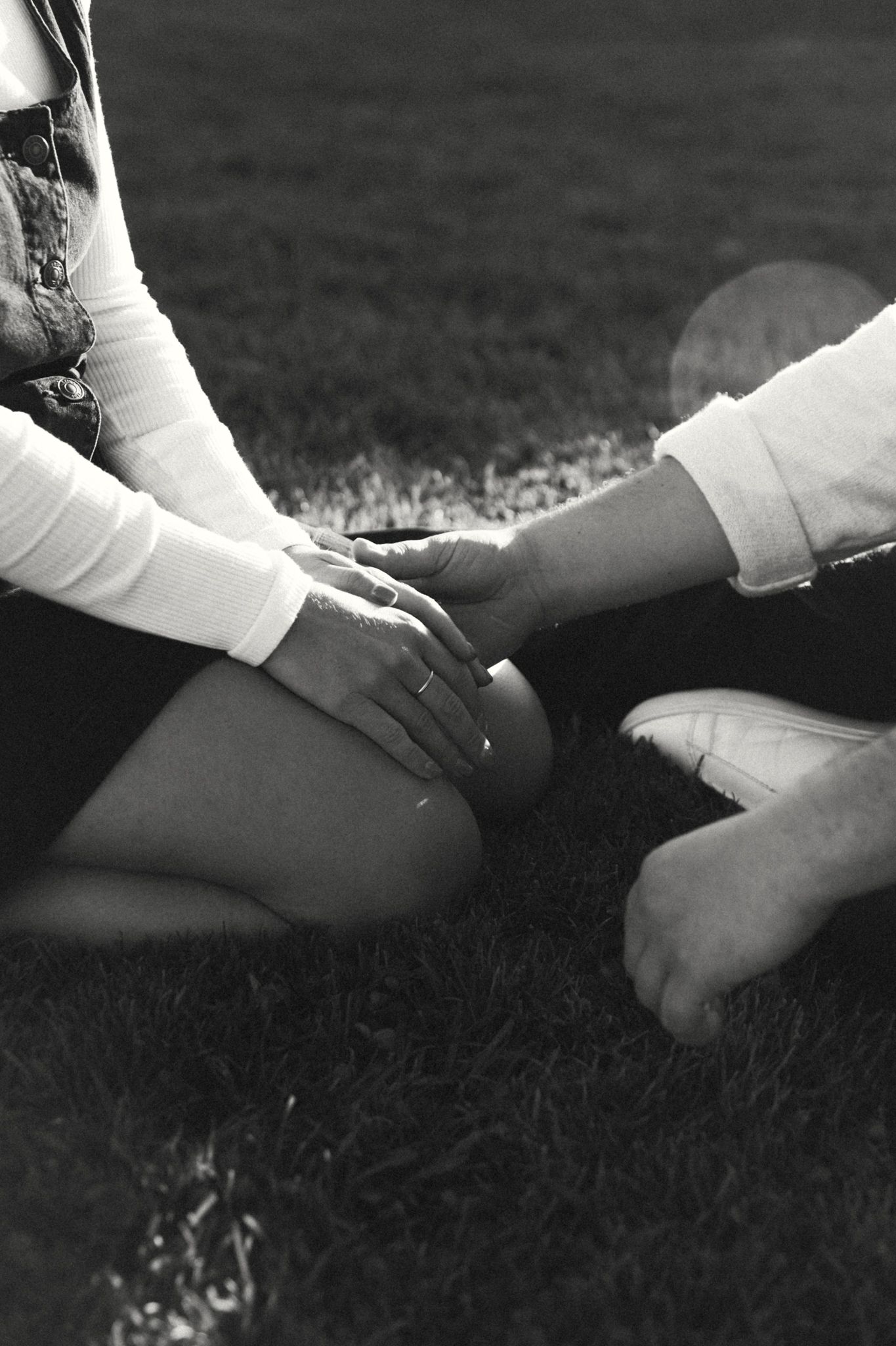 Black and white close-up of hands resting on legs in grass.