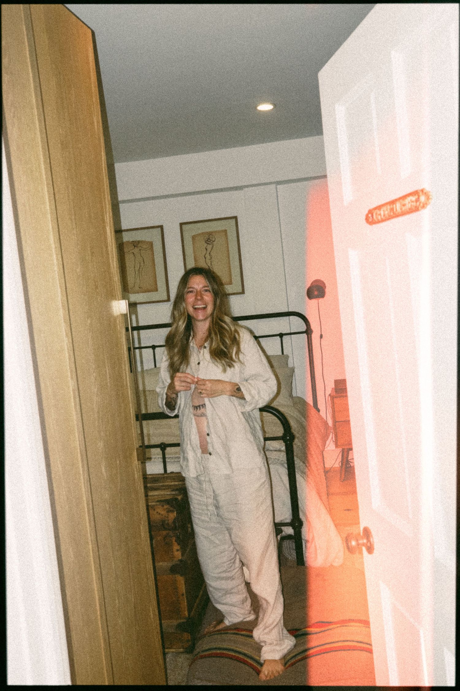 Someone in white overalls playfully poses in a hallway with pink lighting.
