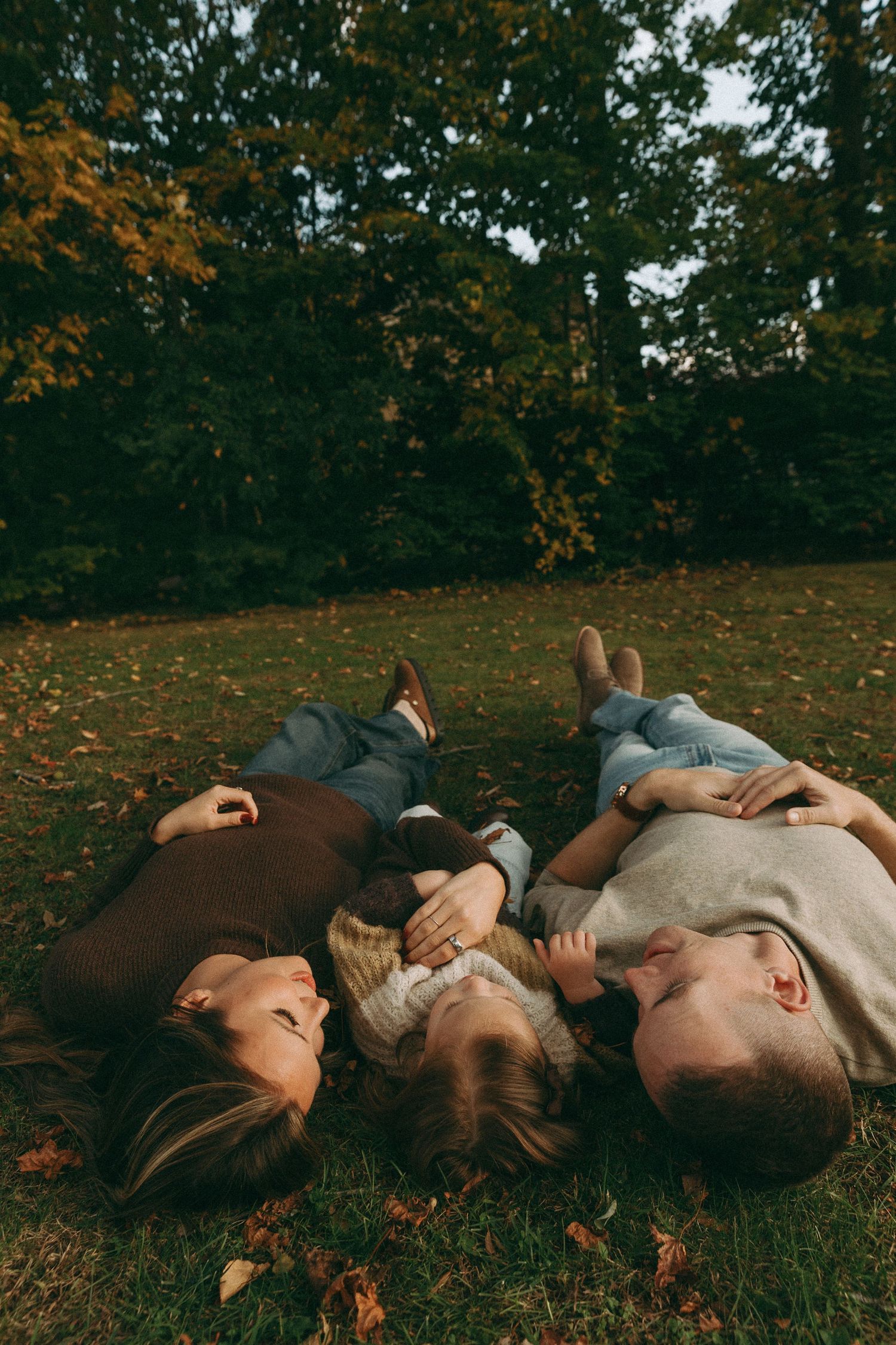 Family of three lying on autumn grass in a park, smiling and bonding together on a fall day.