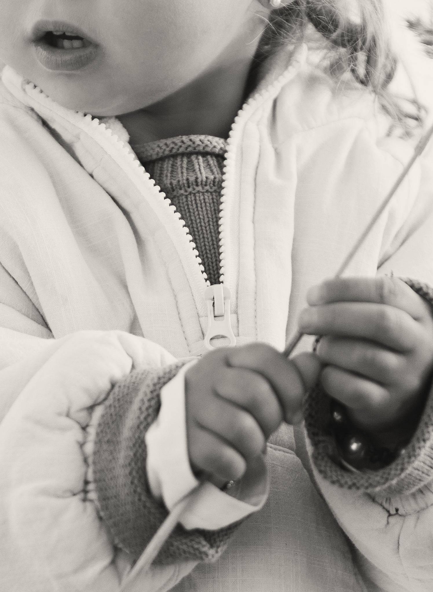 Close-up black and white photo of toddler in white jacket holding small object with tiny hands.