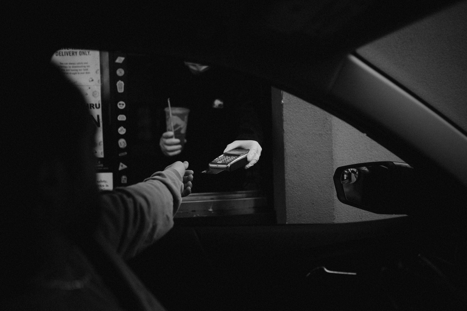A dark image of a hand reaching through a car window at a drive-through window.