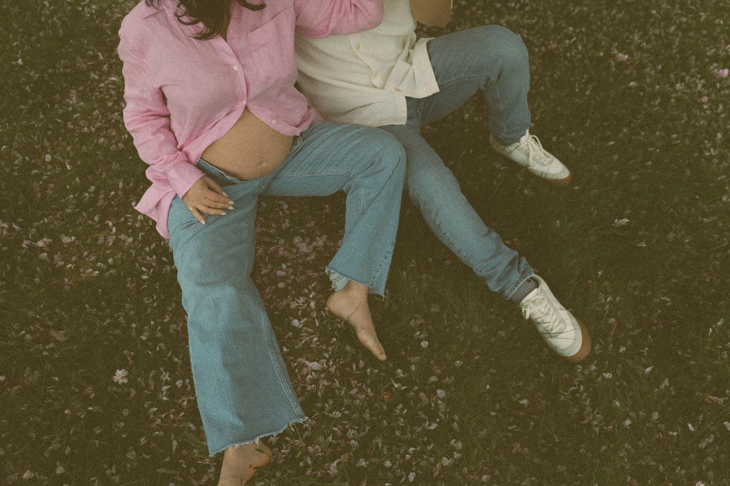 Close-up view of two people's legs standing together on grass under cherry blossoms.