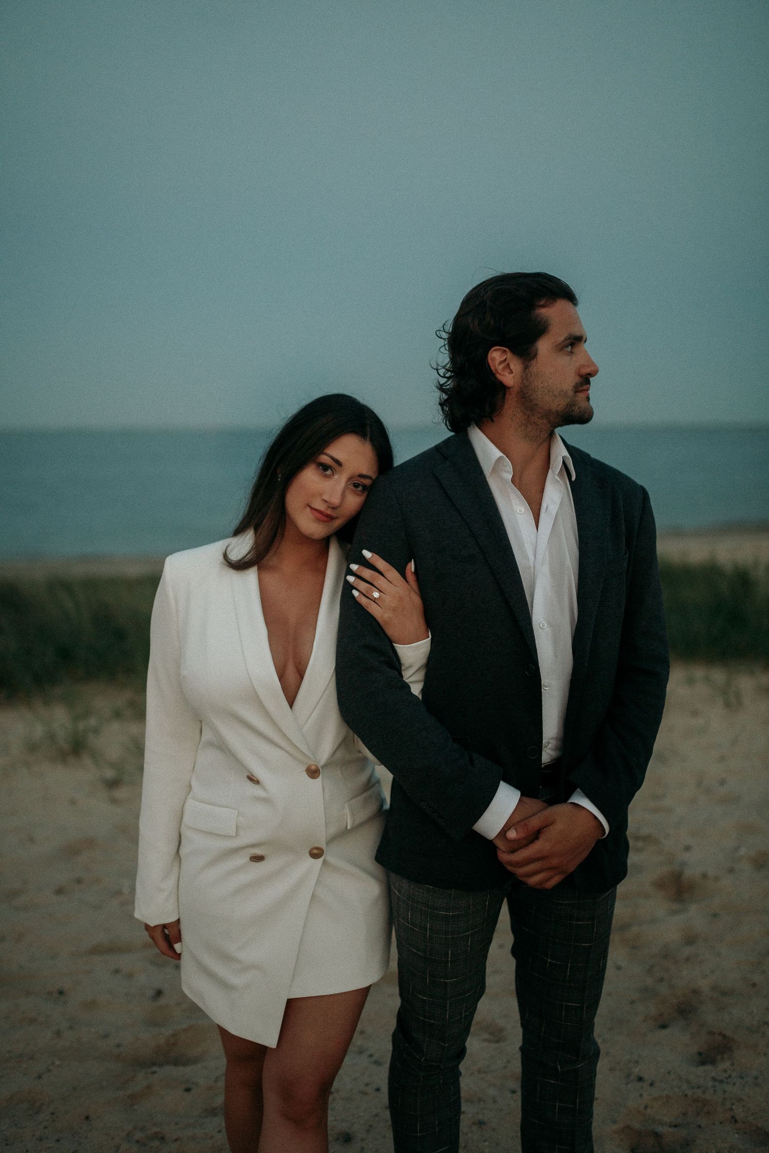 Couple in contrasting black and white outfits posing against a moody coastal backdrop.