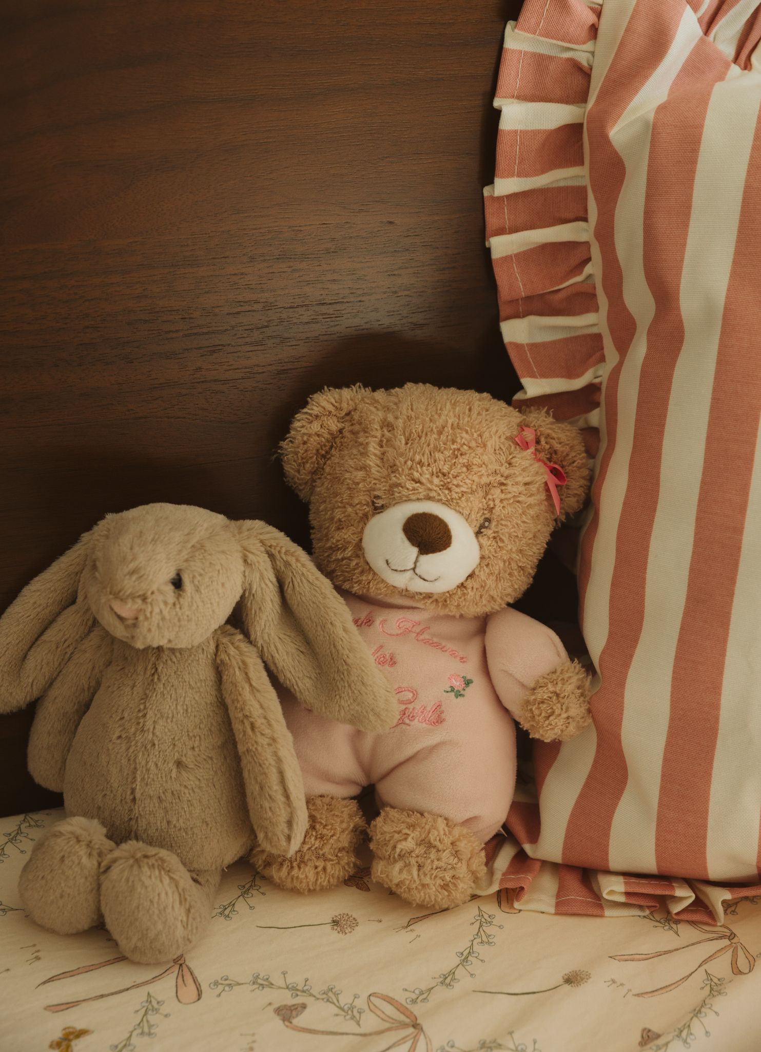 Plush teddy bears and stuffed bunnies arranged with pink striped pillows.