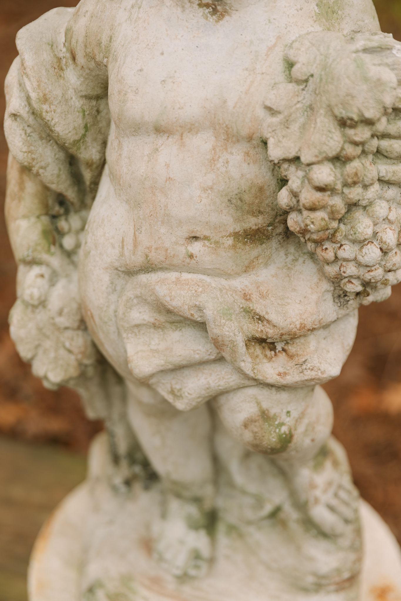 Close-up details of weathered stone cherub statue with moss patina.