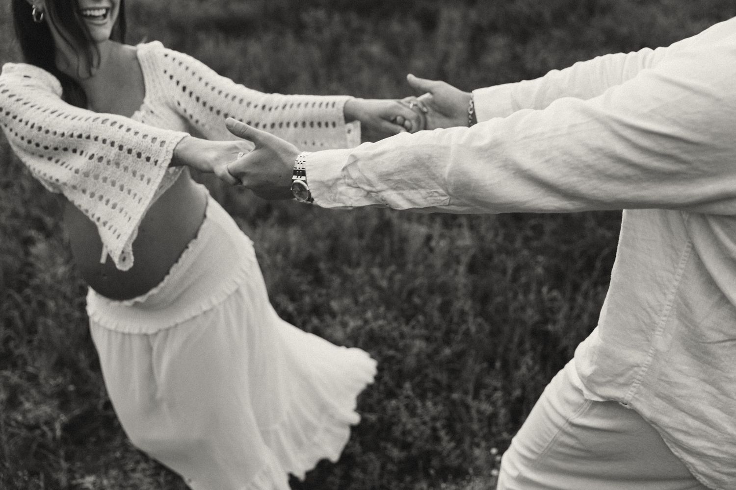 A couple in white clothing spins and dances together in black and white photography.