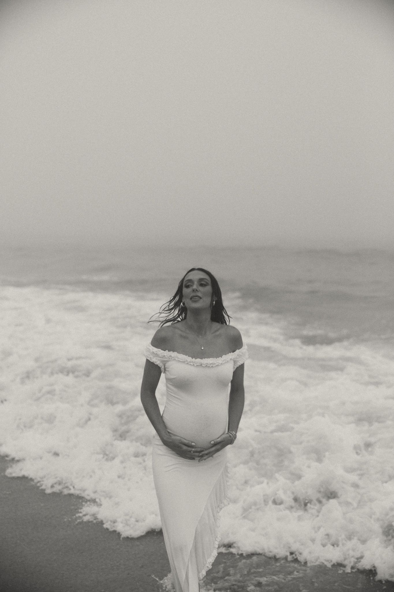 Person in white dress poses against dramatic ocean waves backdrop.