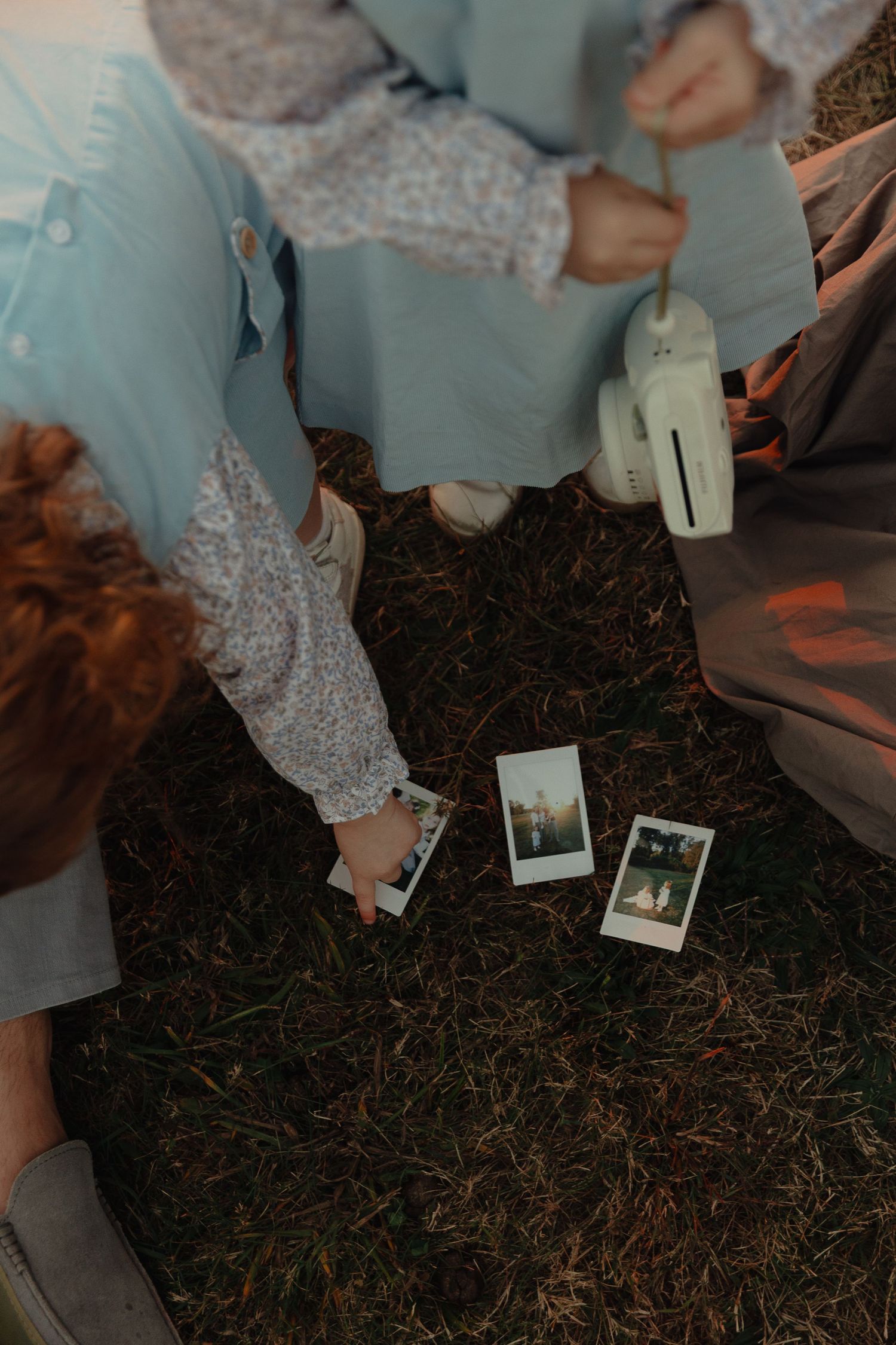 Two people examine freshly developed Polaroid photos on the ground while holding an Instax camera.