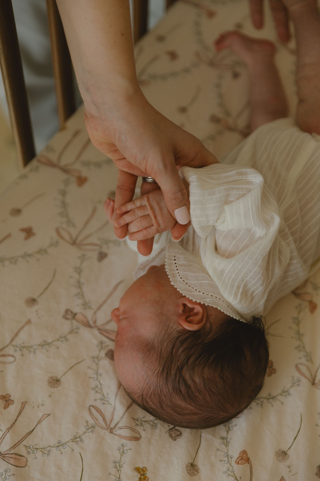 Gentle hands caressing a sleeping infant on floral patterned bedding.