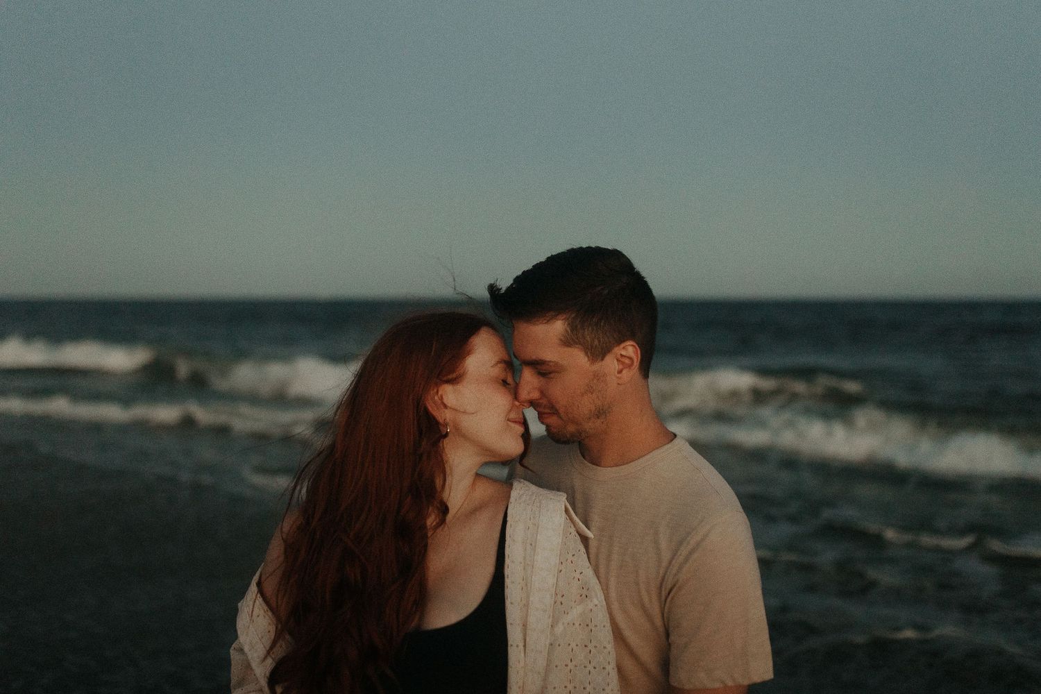 An intimate moment between two people on a moody beach at dusk.