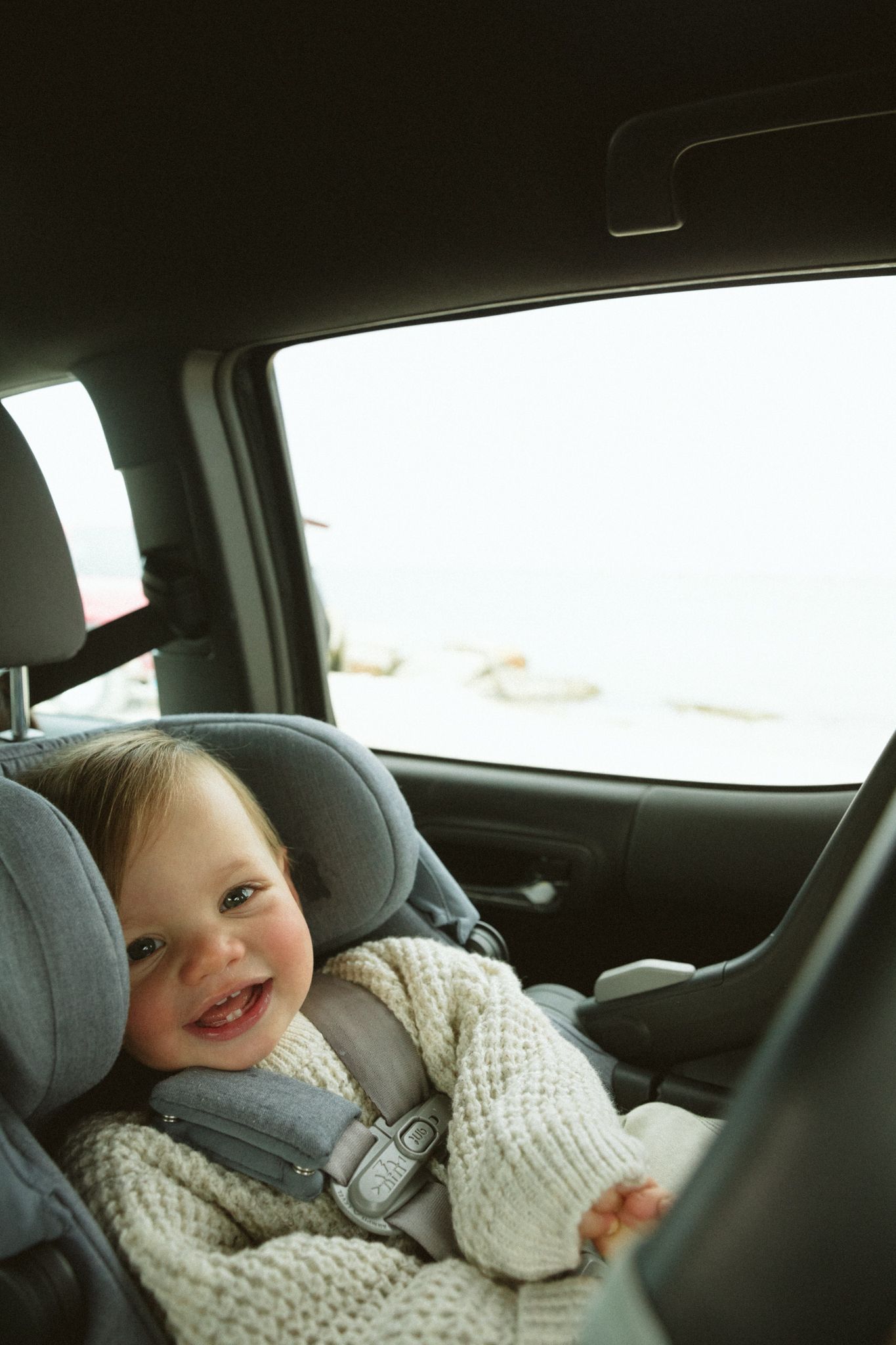 A child looking happy and comfortable while riding in a car seat.