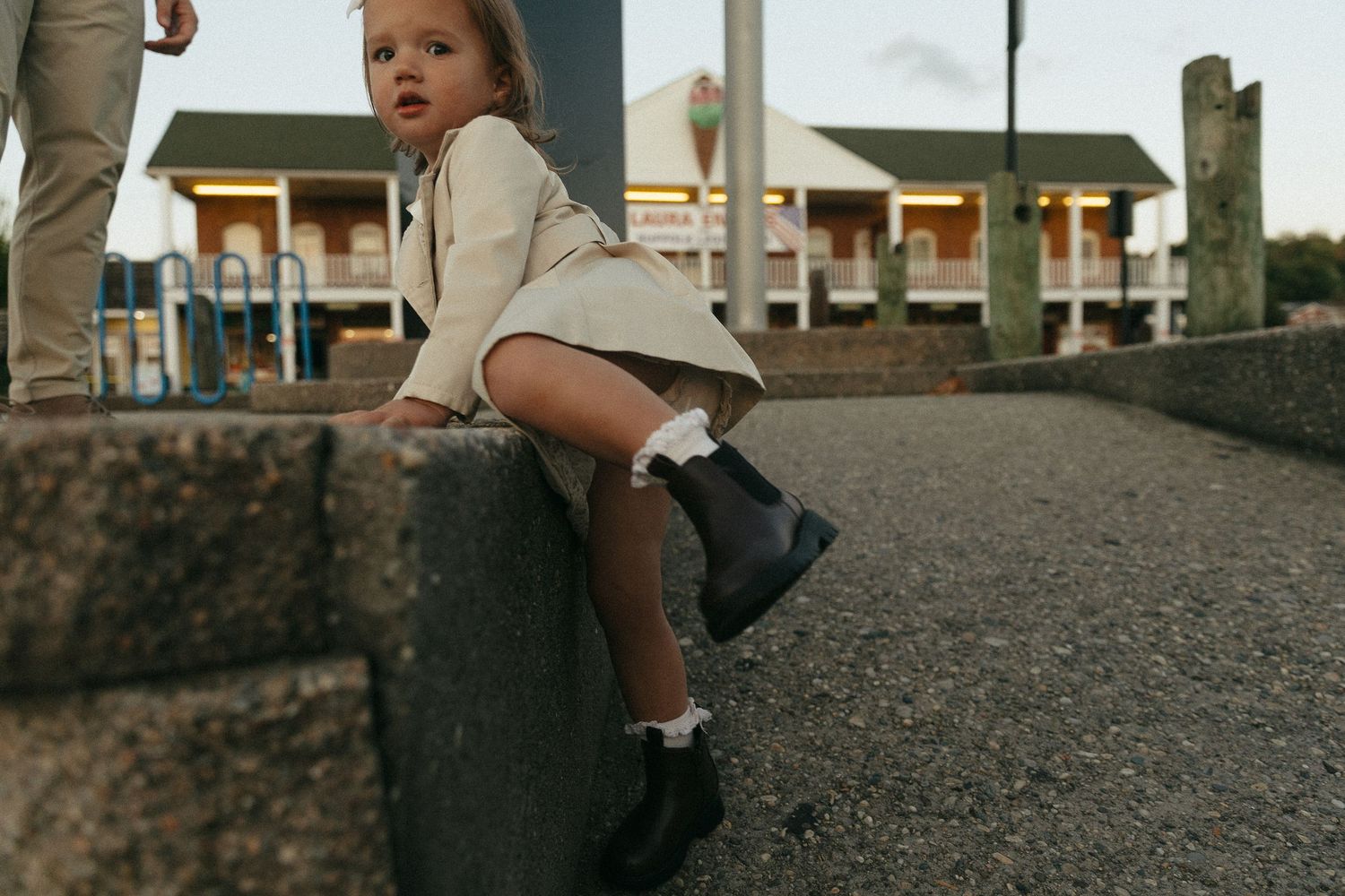 A beige coat and brown boots visible against a gravel surface.
