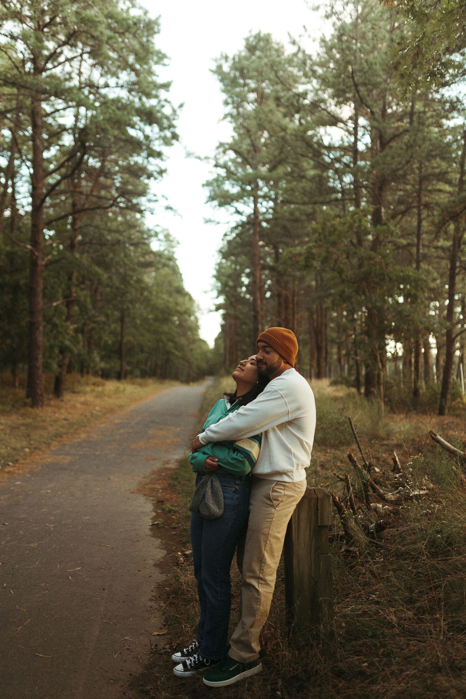 Couple embracing on a forest path surrounded by tall pine trees in a tender romantic moment.