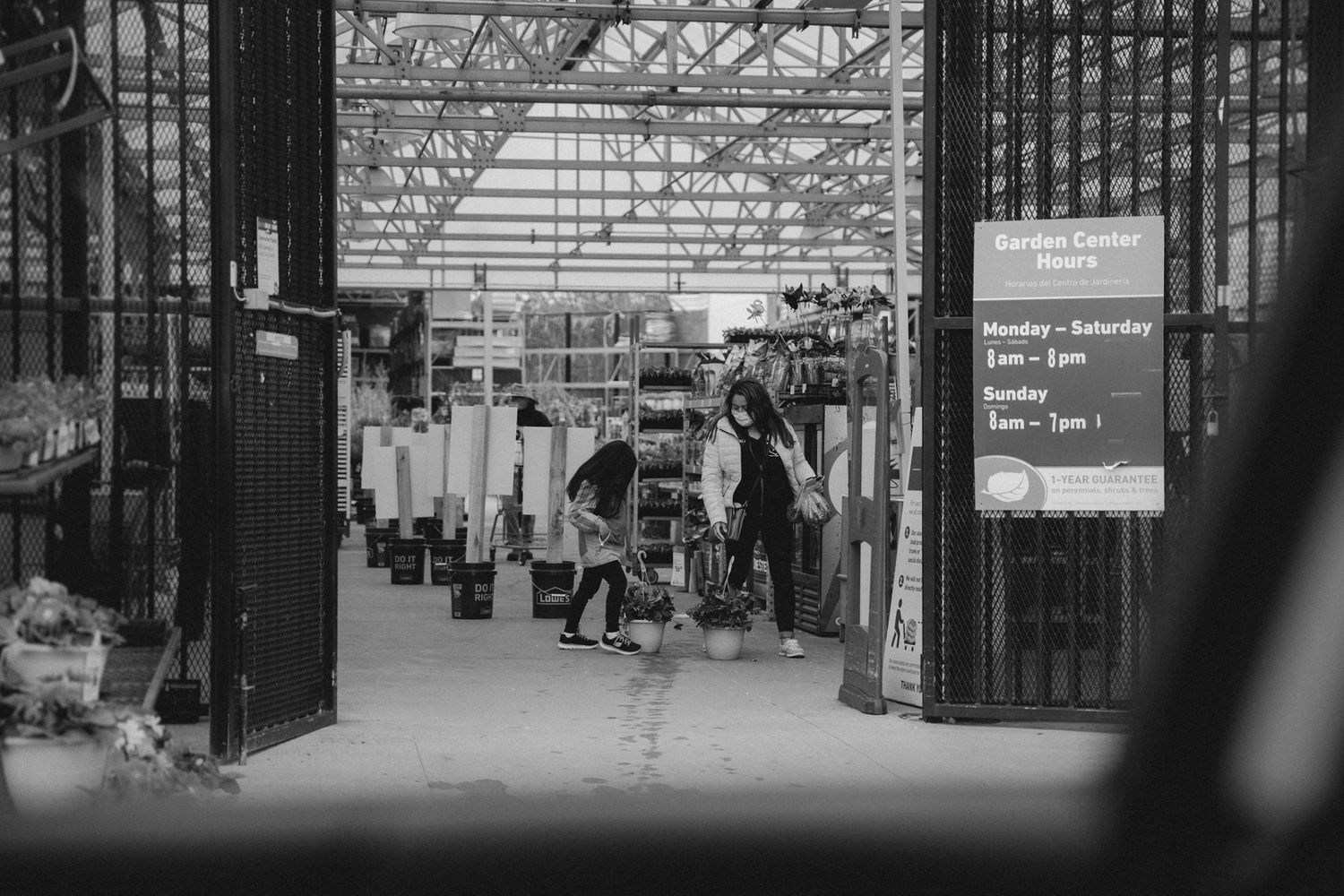 Black and white view of a covered walkway with people walking through metal gates and railings.