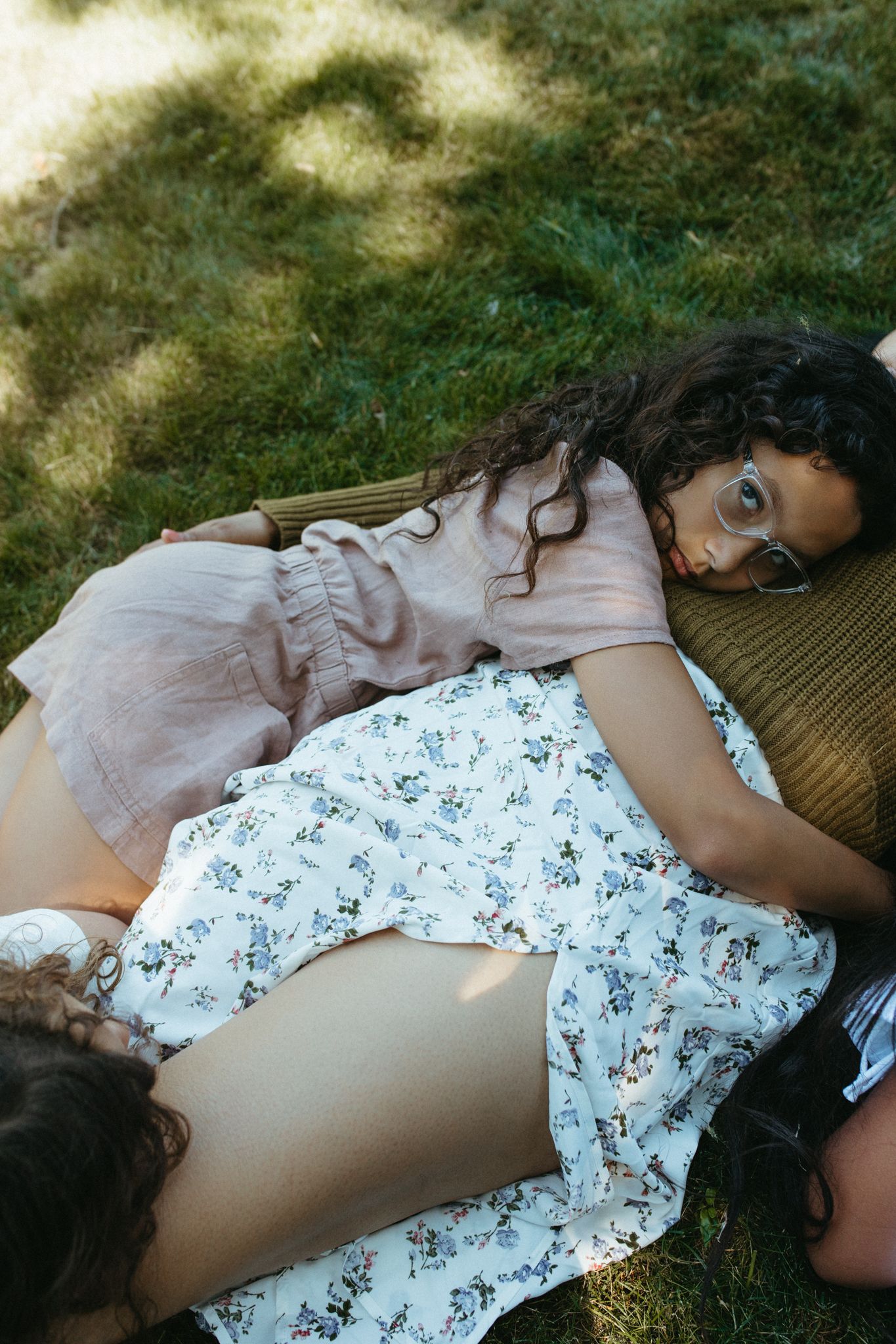 Two people lying on a blanket in the grass on a sunny day wearing floral and pink dresses.