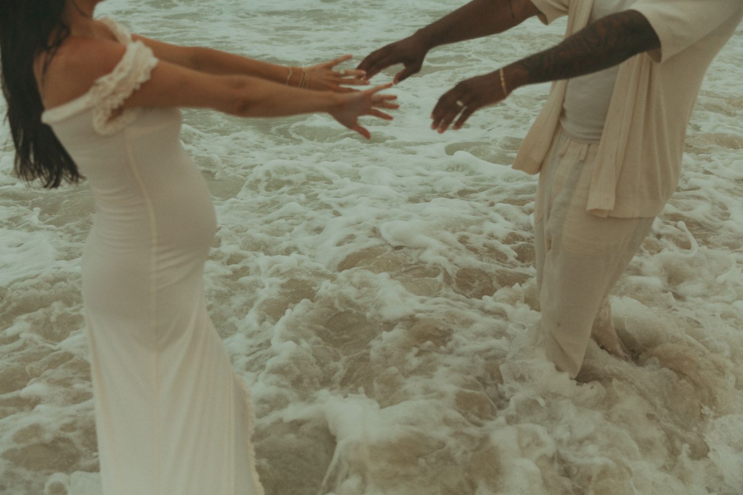 People walking through ocean waves in flowing white clothing.