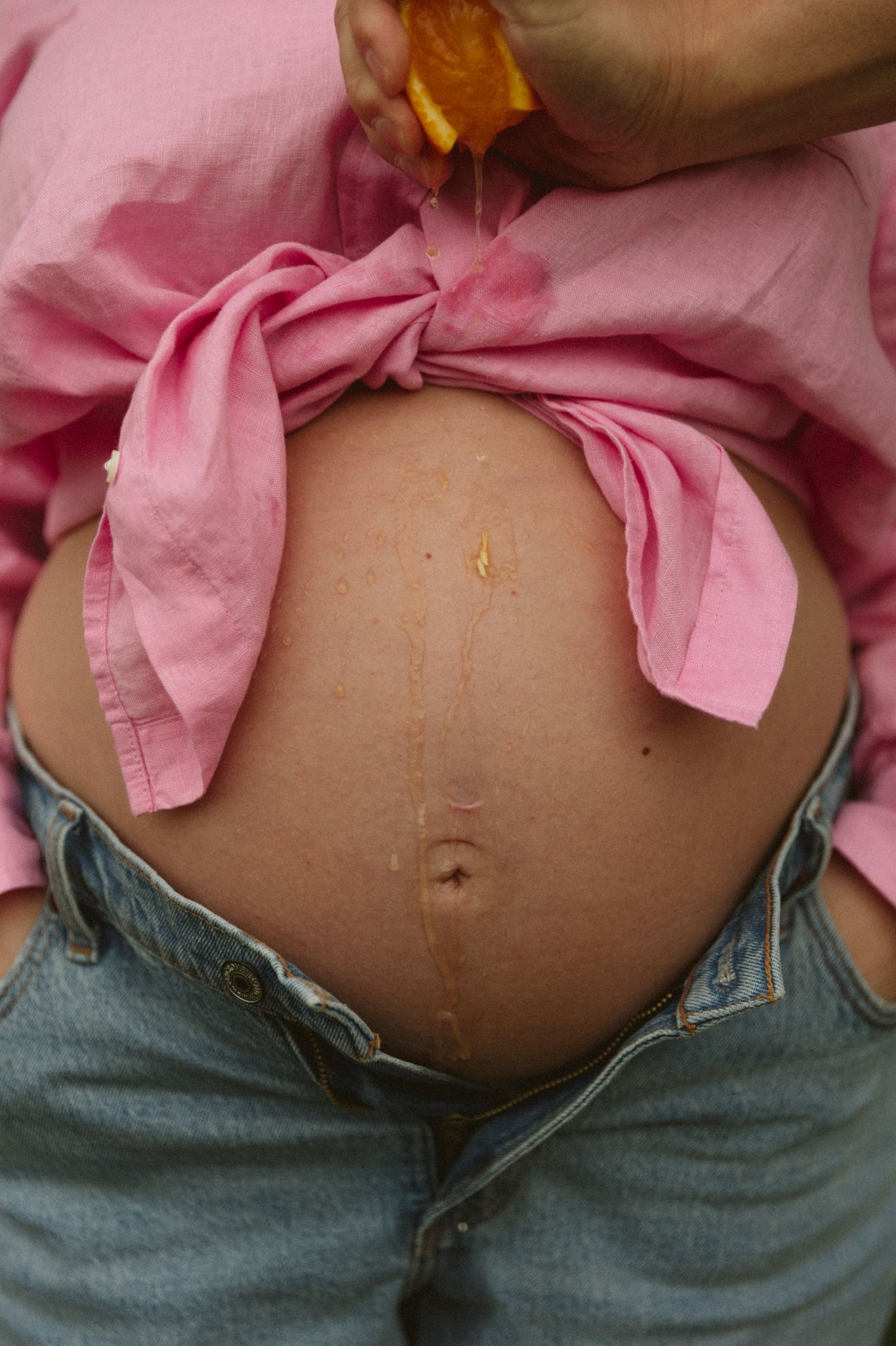 Close up of a pregnant belly with a pink shirt and jeans.