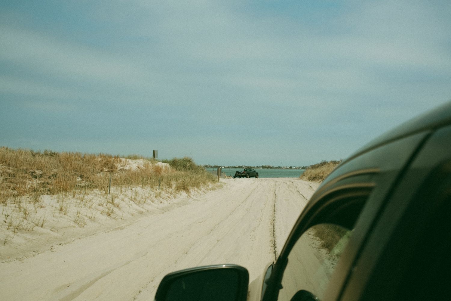 Sandy beach road winding through coastal dunes under blue sky.
