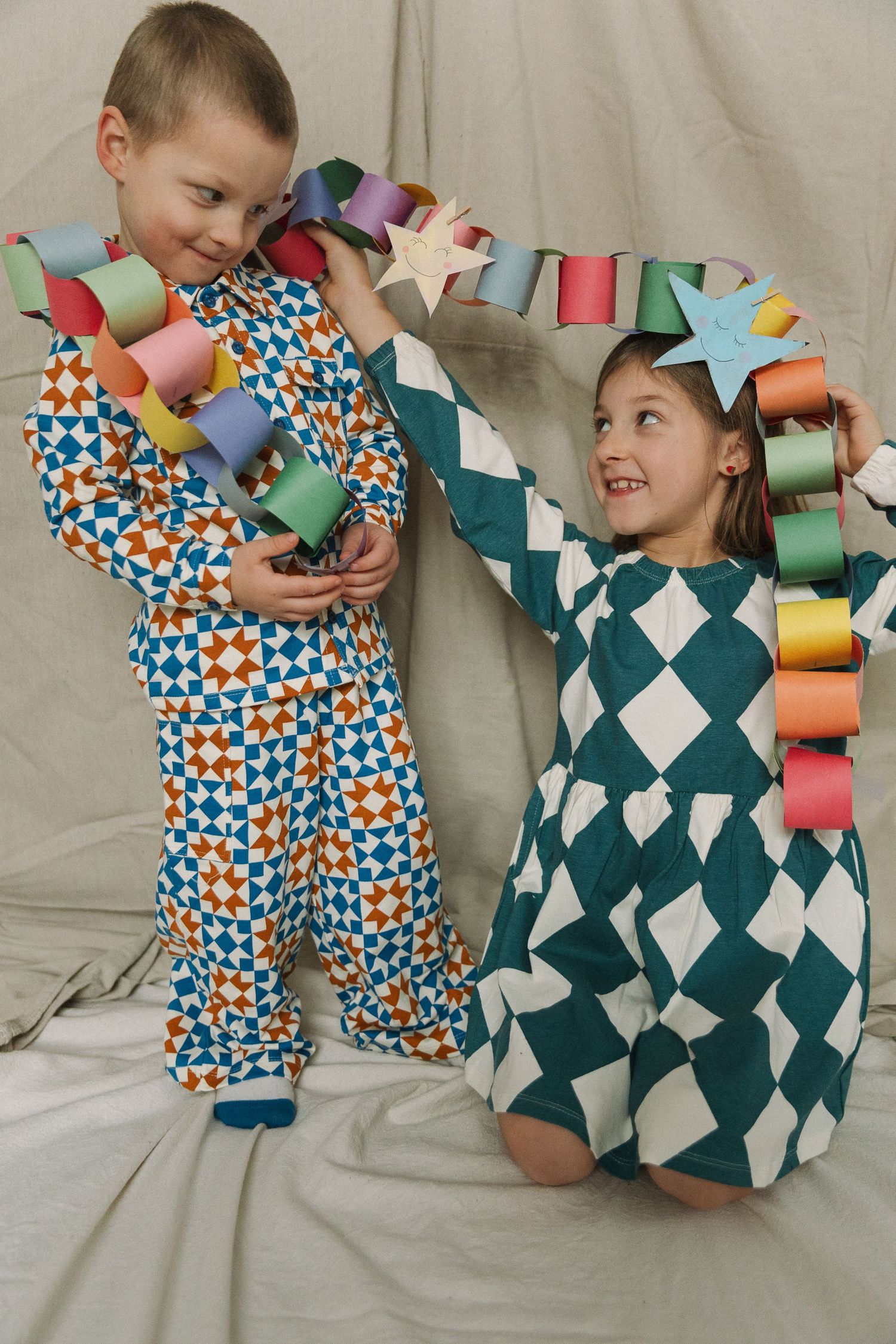 Two children in colorful patterned pajamas holding a paper chain garland with stars, smiling together.