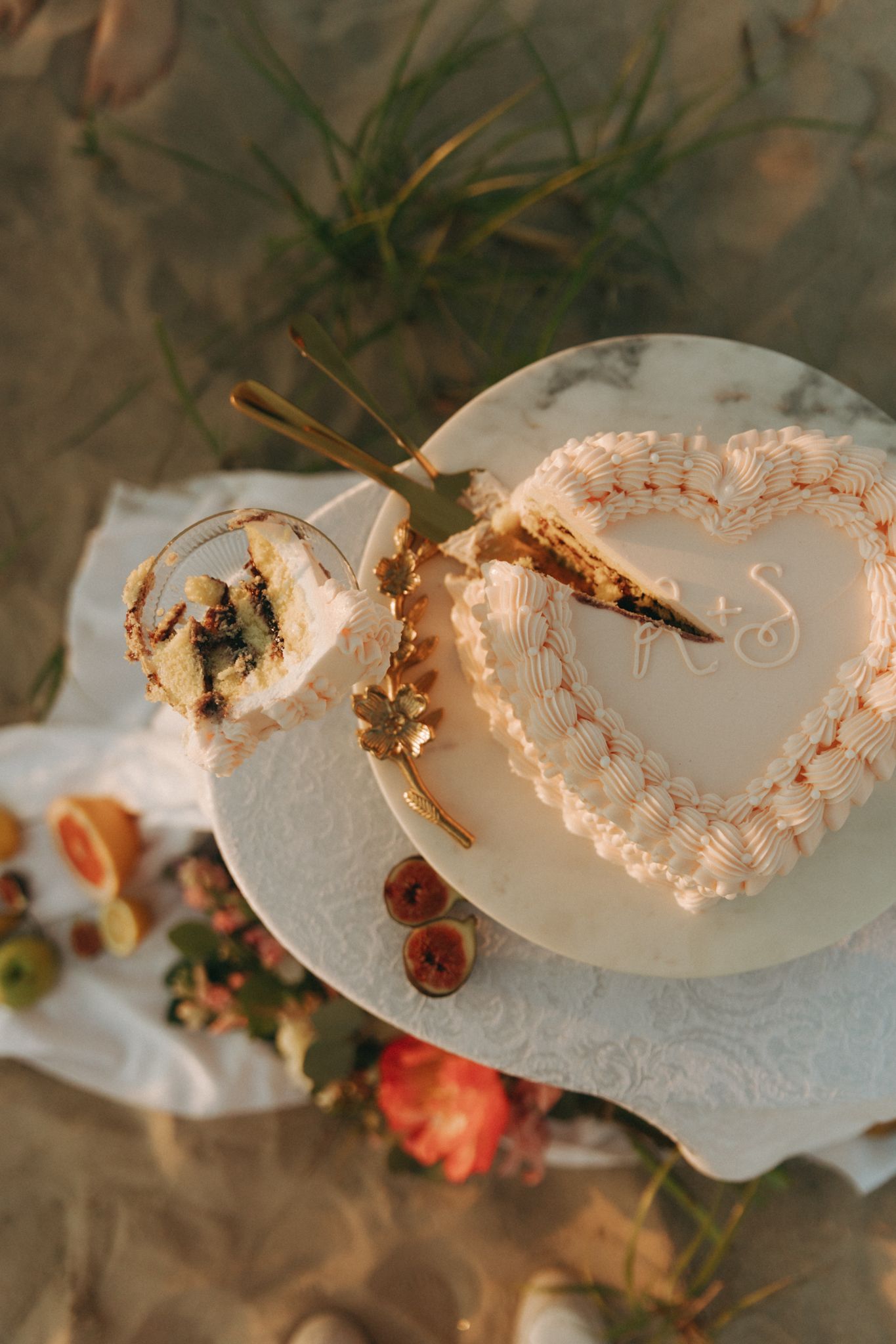 Heart-shaped wedding cake with white frosting and initials, partially sliced, displayed on marble plate with gold cake server.